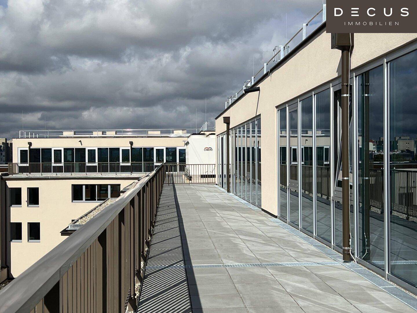 Geräumige Dachterrasse mit Fliesenboden, Glasfront und Blick auf die Umgebung.