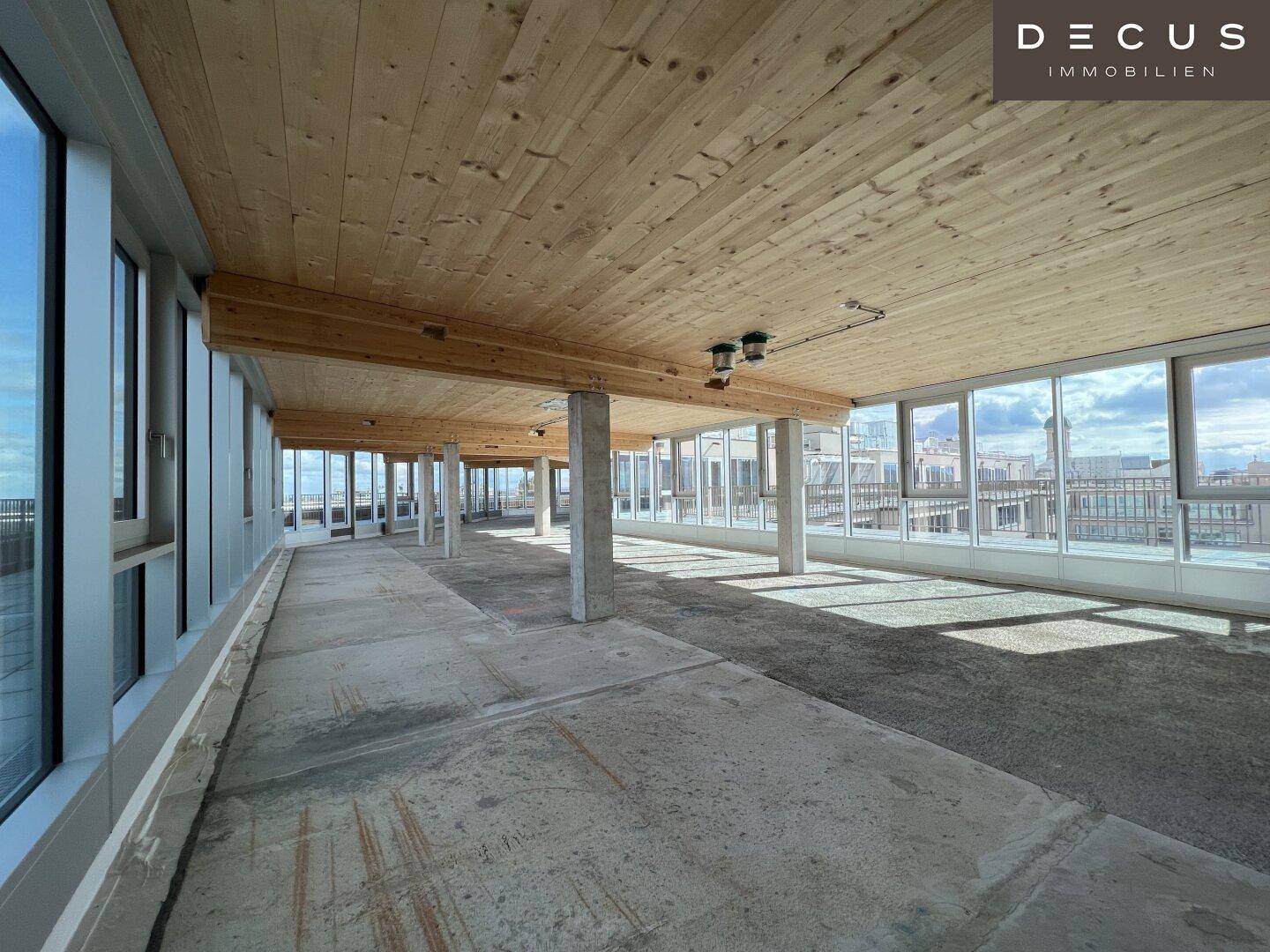 Heller Gewerberaum im Rohbau mit Holzbalkendecke und durchgehenden Fensterfronten.
