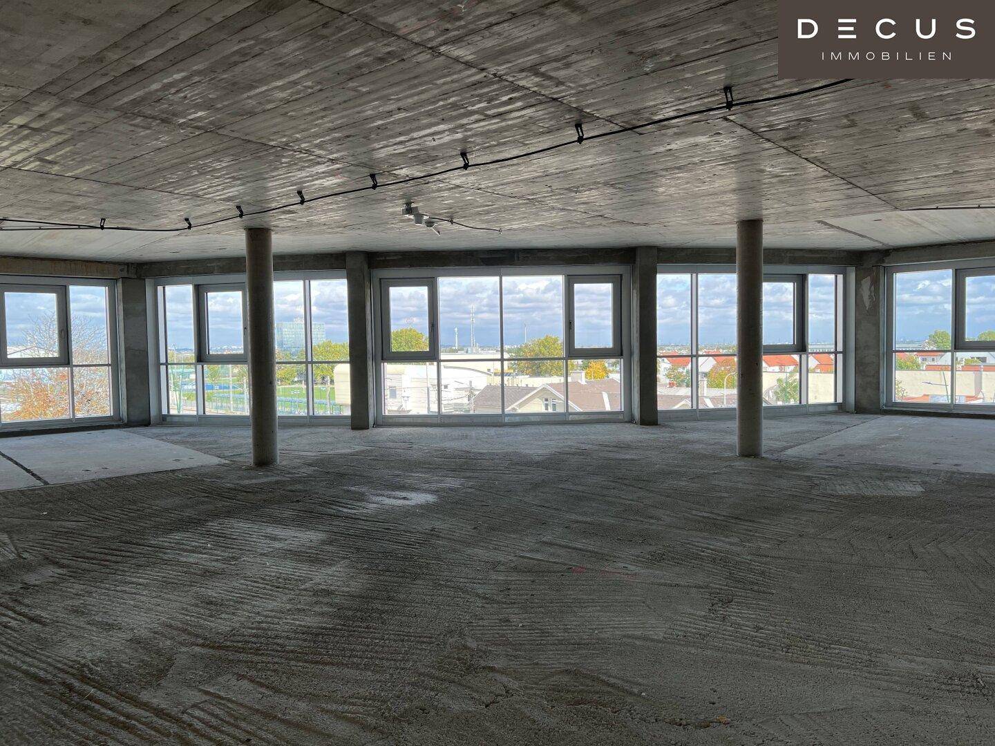 Offener Gewerberaum im Rohbau mit Betonboden, Betondecke und vielen Fenstern.
