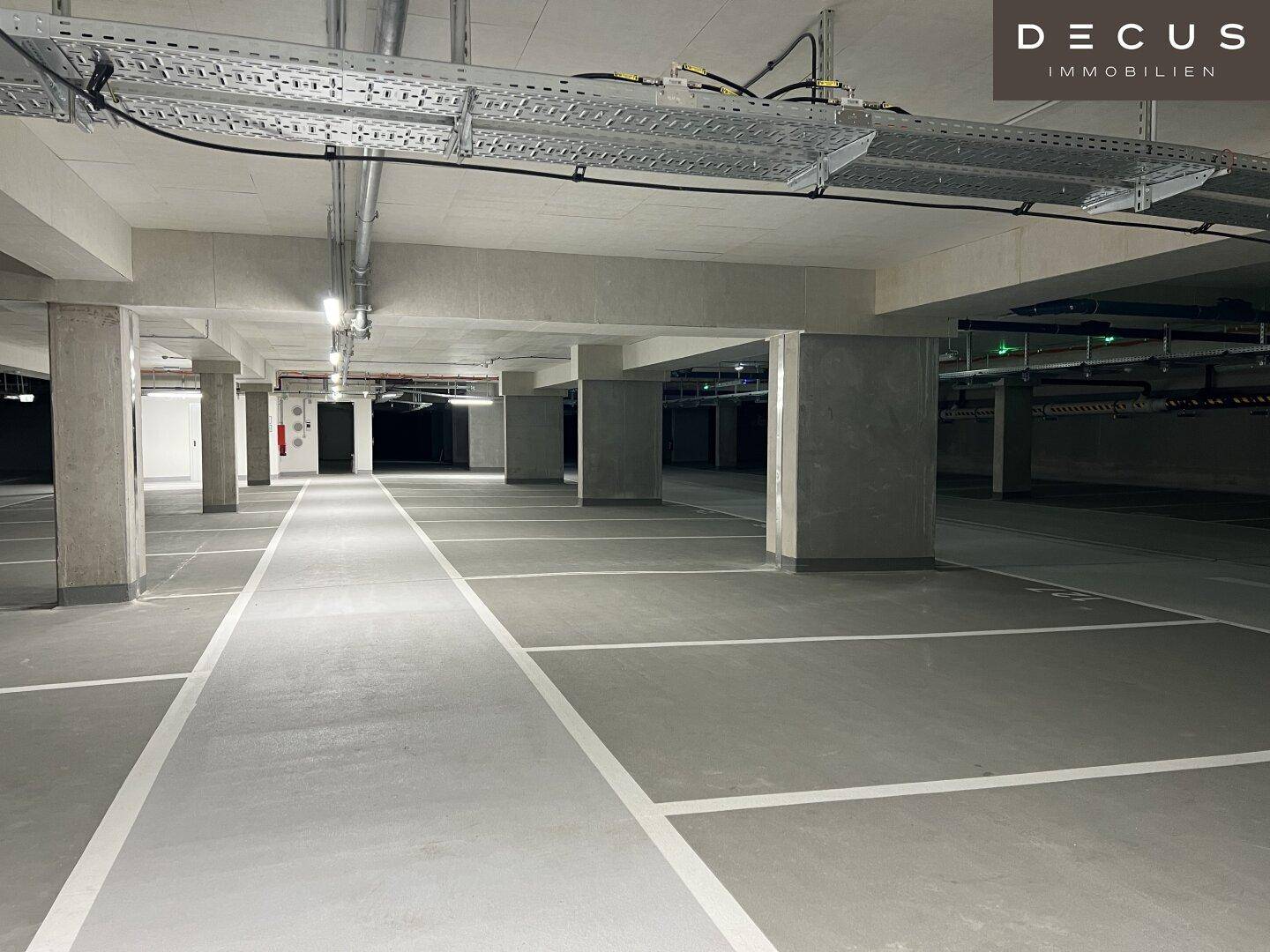 Geräumige Tiefgarage mit markierten Parkplätzen und sichtbaren Installationen an der Decke.