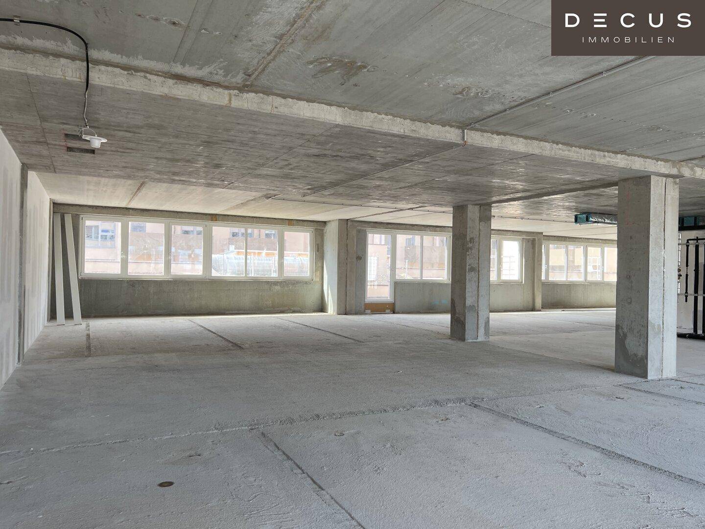 Großer, offener Gewerberaum im Rohbau mit Betonboden und vielen Fenstern.
