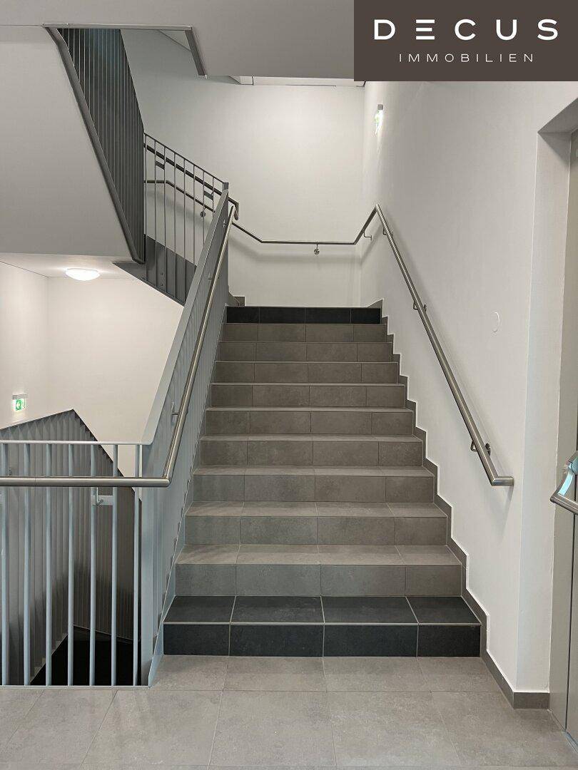 Geräumiges Treppenhaus mit Fliesenstufen und modernen Metallgeländern.