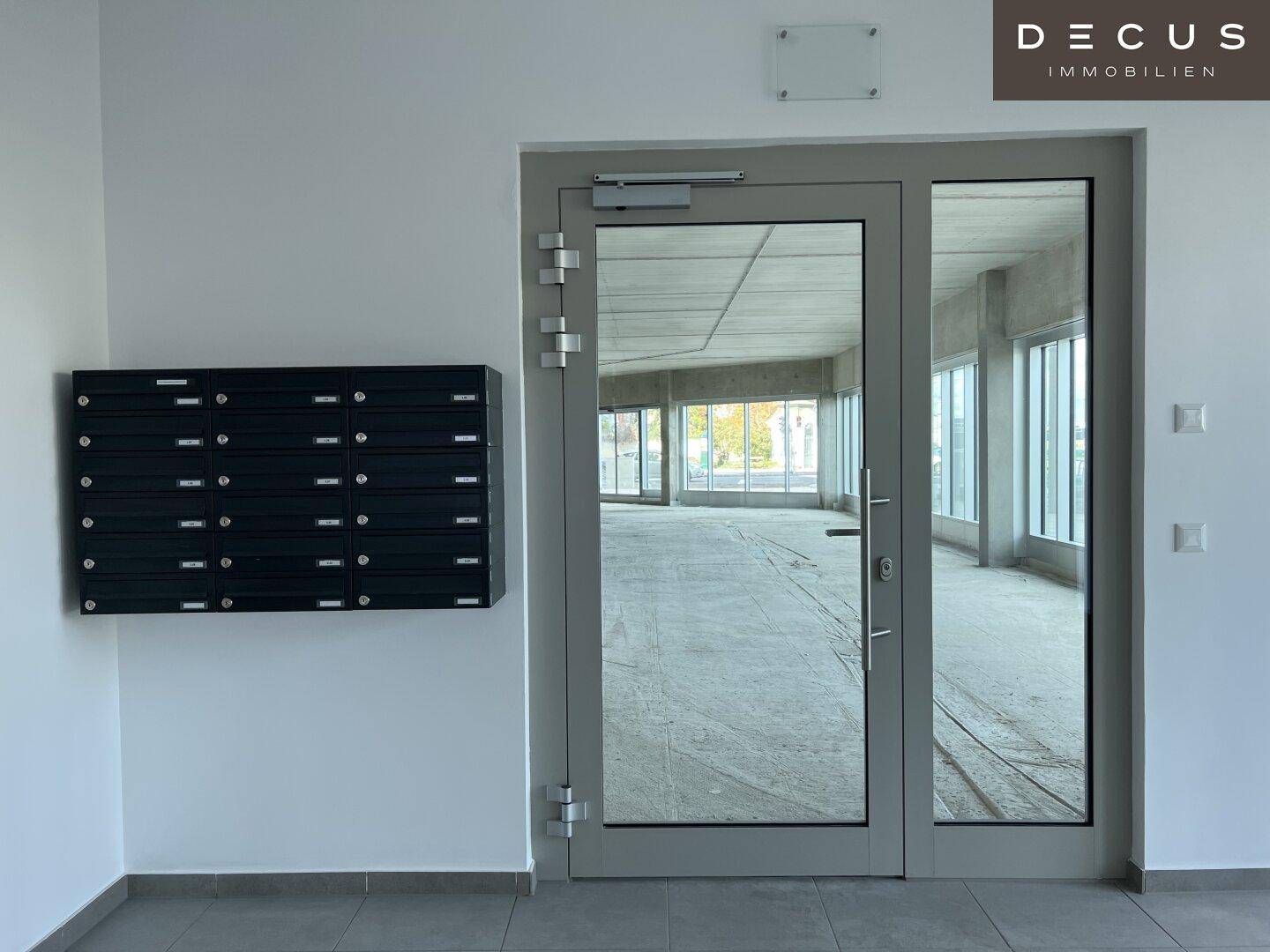 Heller Eingangsbereich mit schwarzer Briefkastenanlage und Blick durch die Glastür in einen Rohbau.