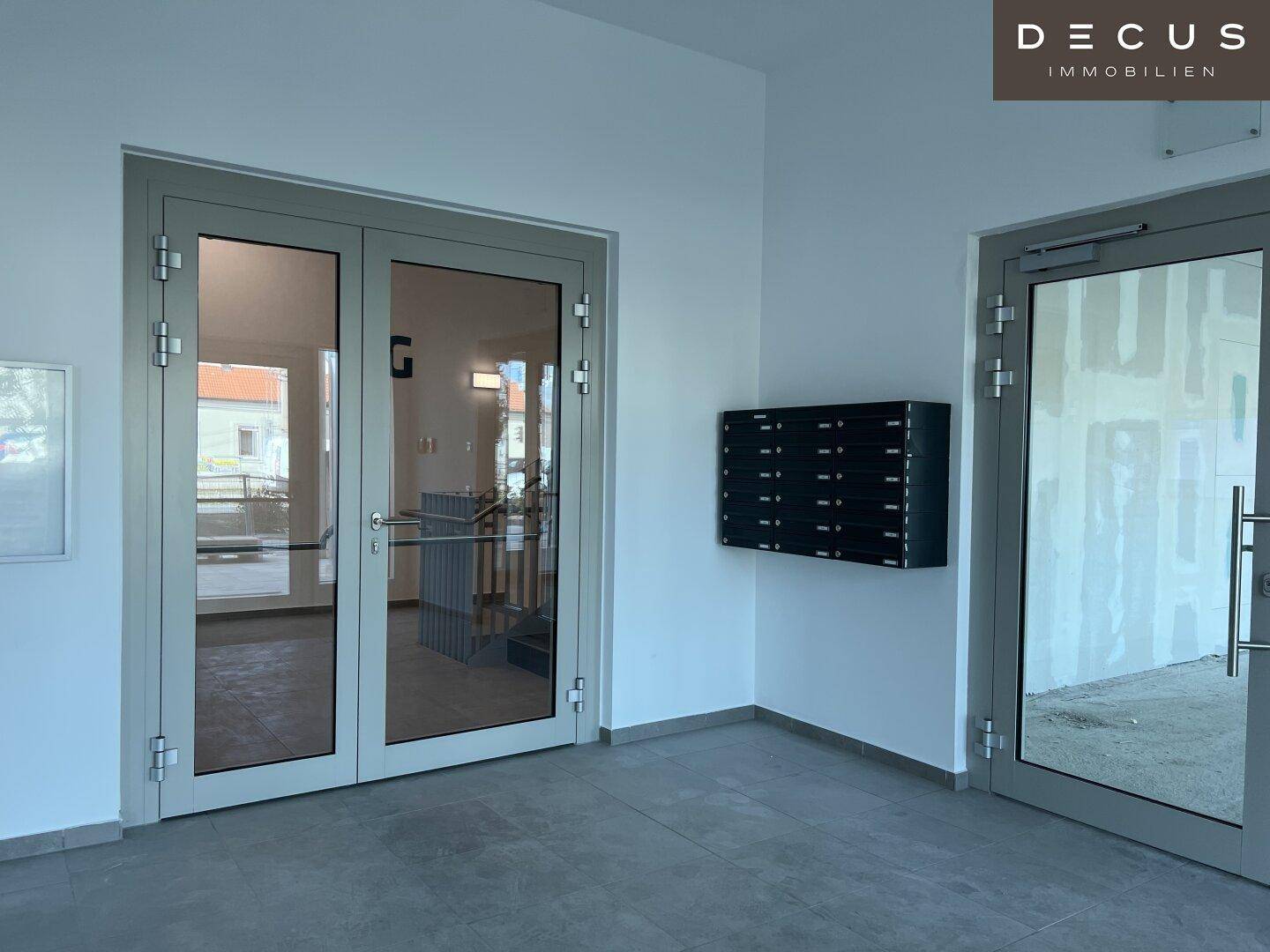 Eingangsbereich mit modernen Glastüren, Briefkästen an der Wand und Fliesenboden.