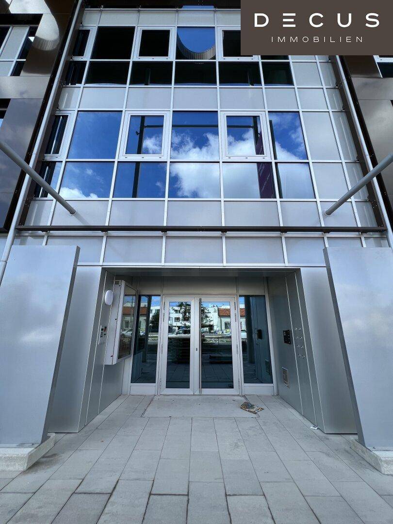 Haupteingang des modernen Gebäudes mit Glasdoppeltüren und reflektierender Fassade.