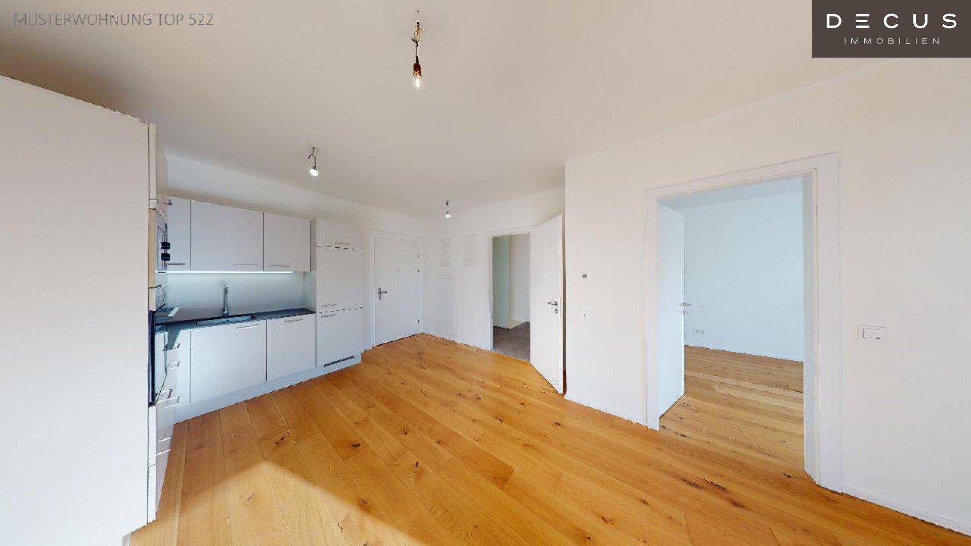 Offene Küche mit weißen Einbauschränken und Holzboden, mit Blick in angrenzende Räume.
