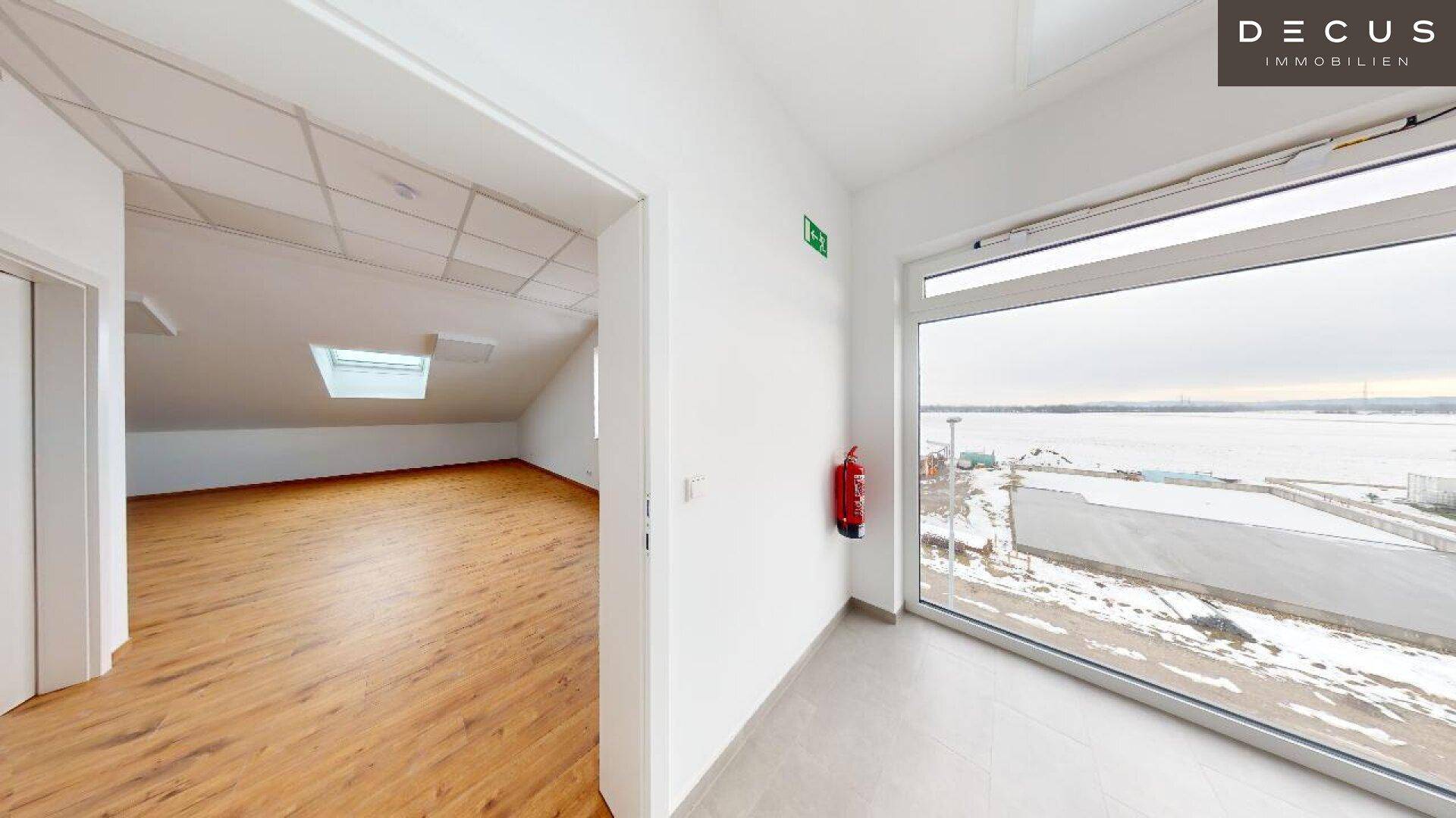 Innenansicht mit zwei Bereichen: ein Raum mit Holzboden und ein gefliester Bereich mit großem Fenster.