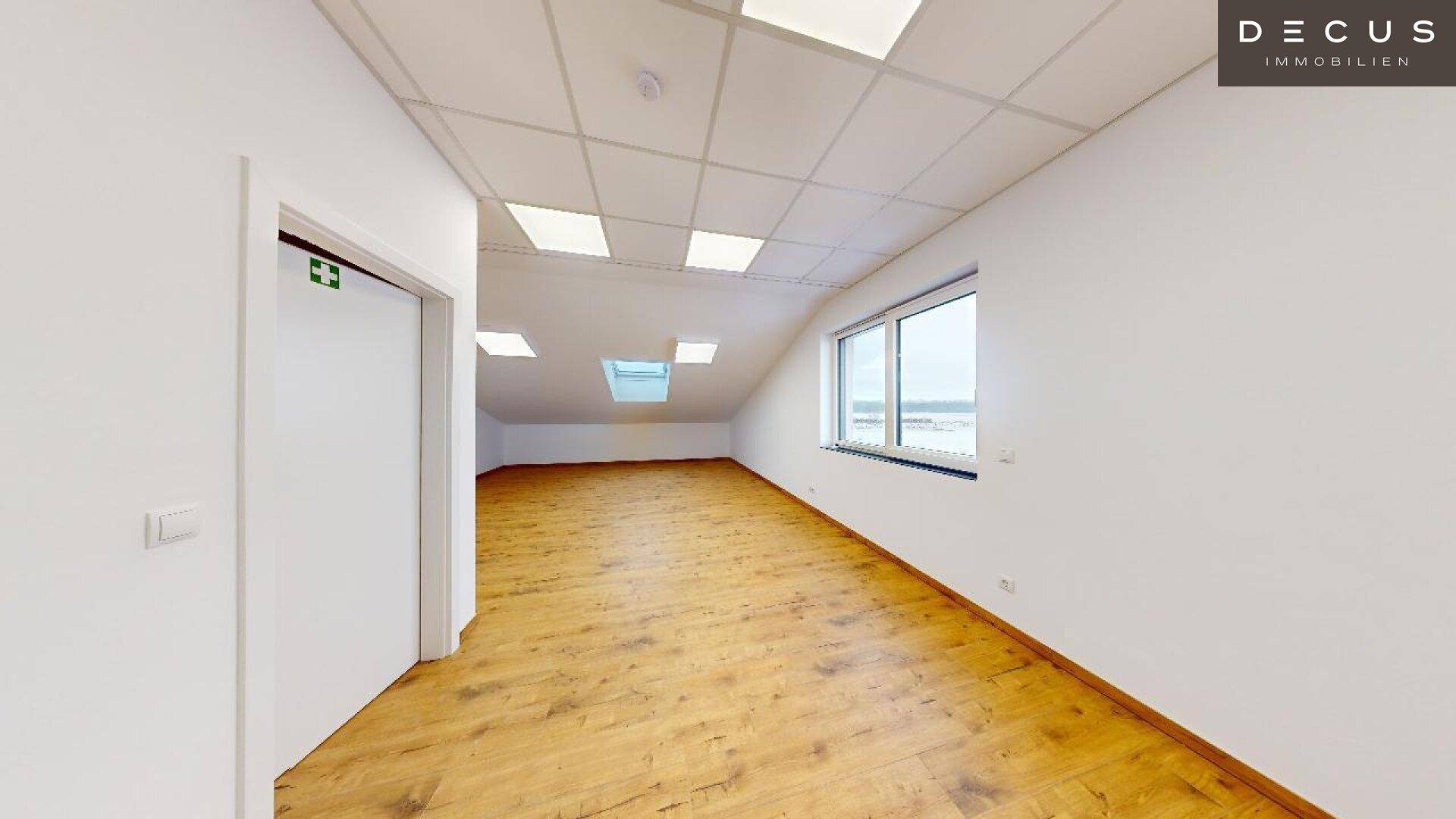Geräumiger Büroraum mit Holzboden, weißen Wänden und Blick auf die verschneite Umgebung.