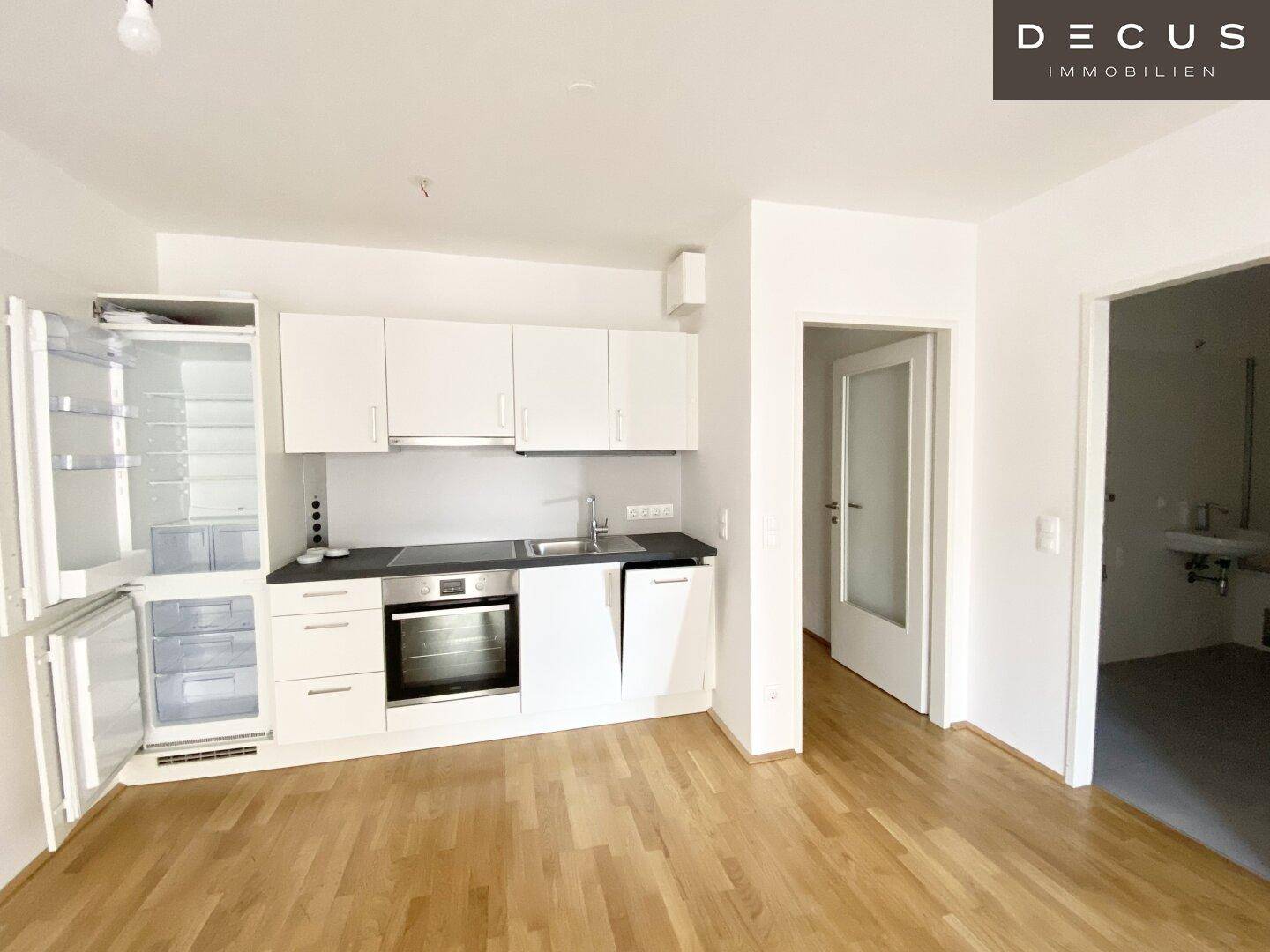 Moderne Einbauküche mit weißen Schränken, dunkler Arbeitsplatte und integrierten Geräten in hellem Raum.