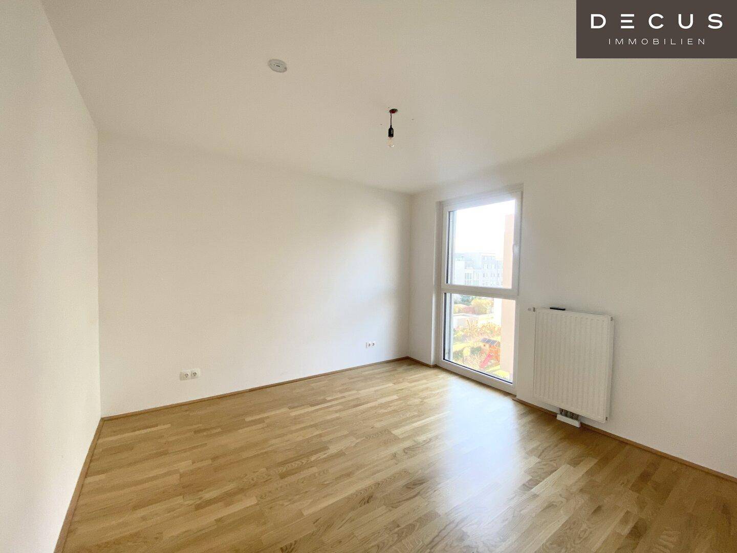Geräumiges Schlafzimmer mit großem Fenster, viel Tageslicht und hellem Parkettboden, unmöbliert.