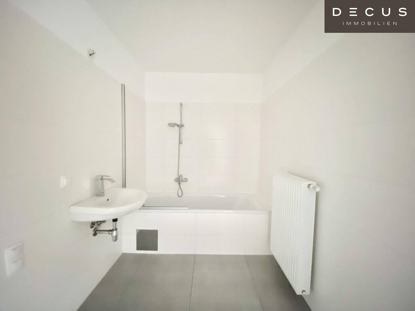 Modernes Badezimmer mit Badewanne, Waschbecken und hellen Fliesen an Wänden und Boden, sehr gepflegt.