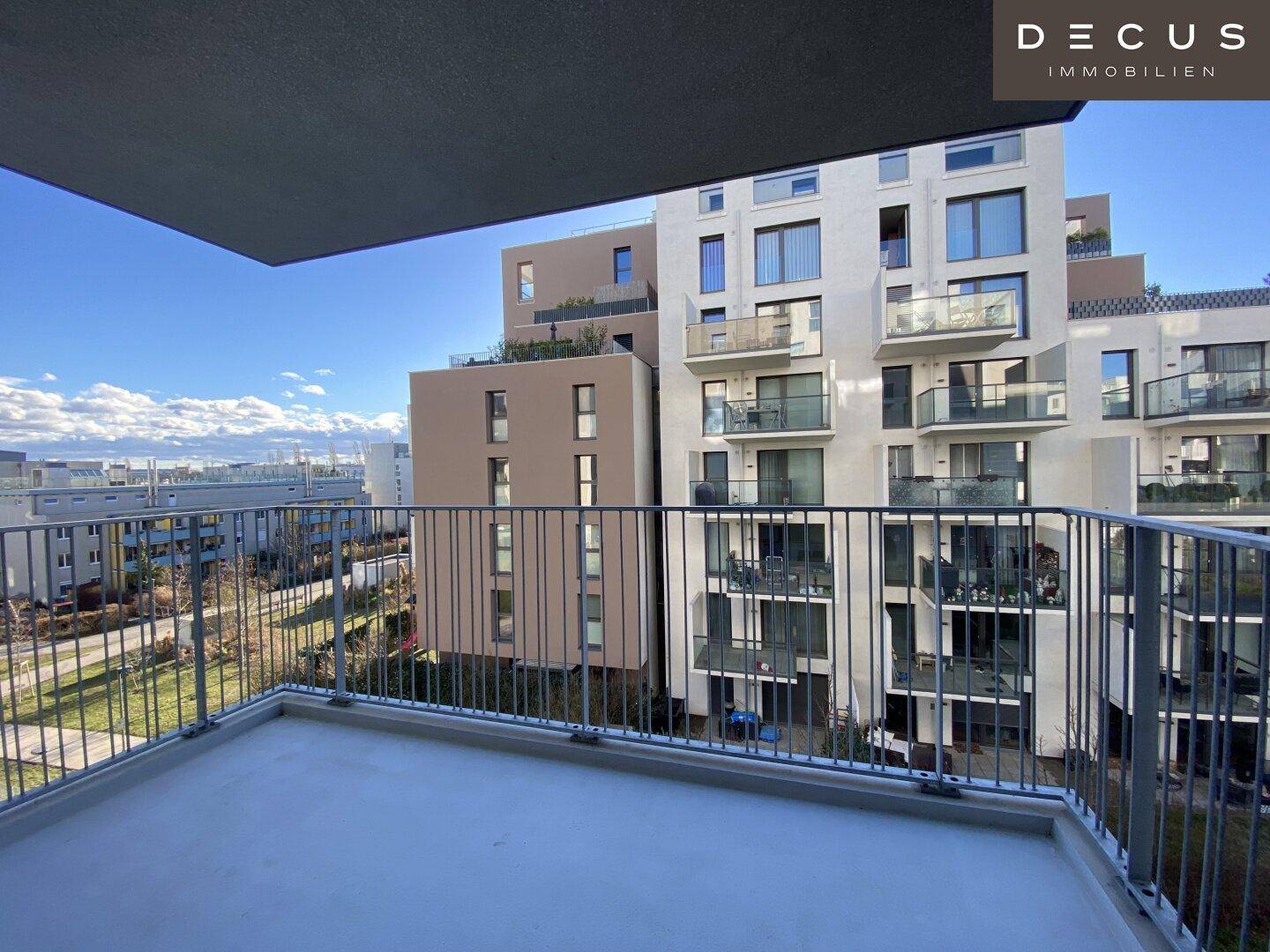 Geräumiger Balkon mit Metallgeländer und Blick auf die umliegenden Gebäude und grüne Flächen.