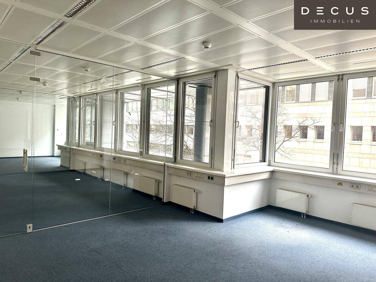 Heller Büroraum mit großen Fenstern, Teppichboden und einer modernen Glaswand.