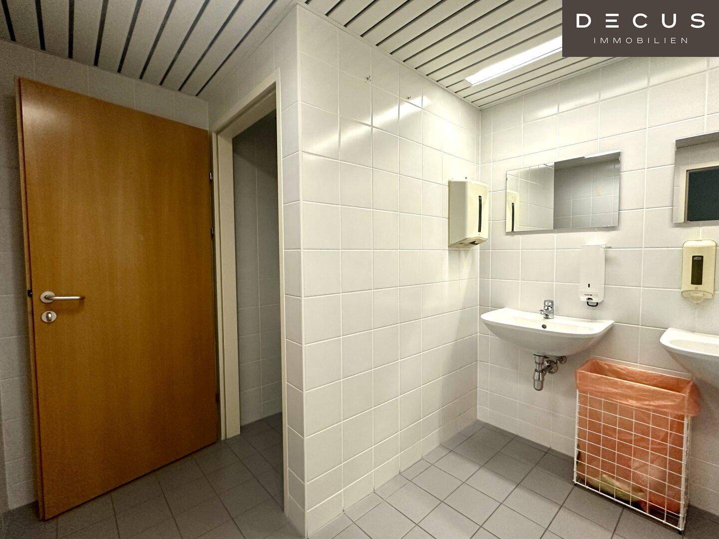 Toilettenraum mit weißen Fliesen, zwei Waschbecken und Spiegelschränken, funktional und sauber.