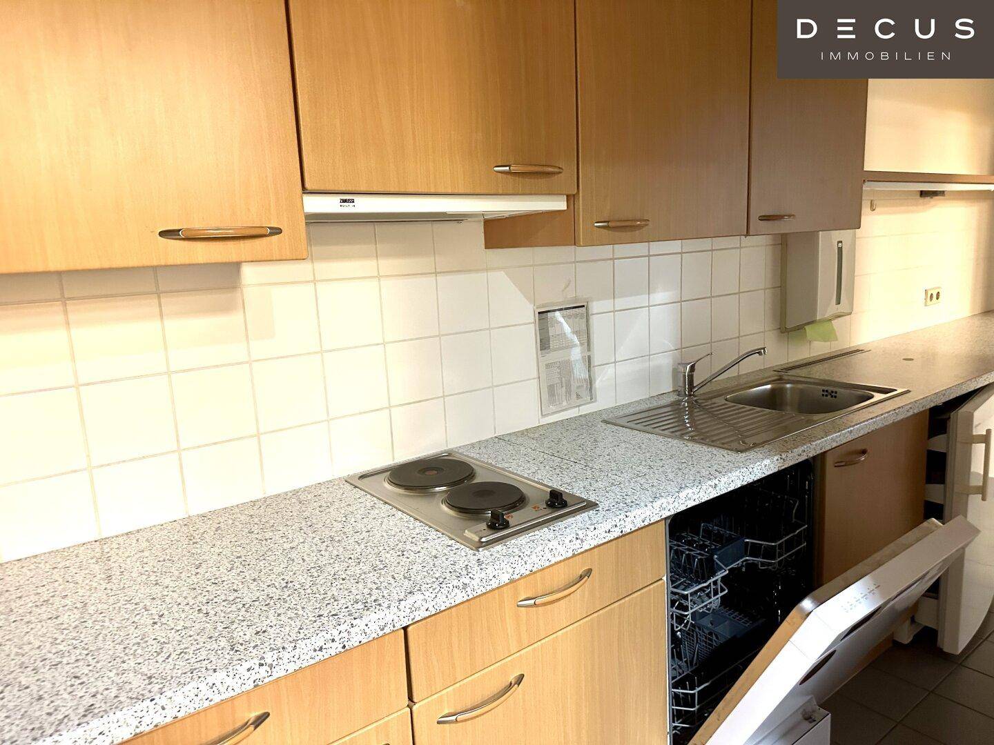 Funktionale Einbauküche mit Holzschränken, Spülmaschine und Elektrokochfeld, ideal für Büronutzung.