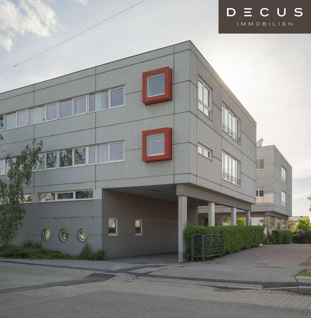 Eckansicht des Bürogebäudes mit markanten roten Fensterrahmen und überdachtem Eingangsbereich.