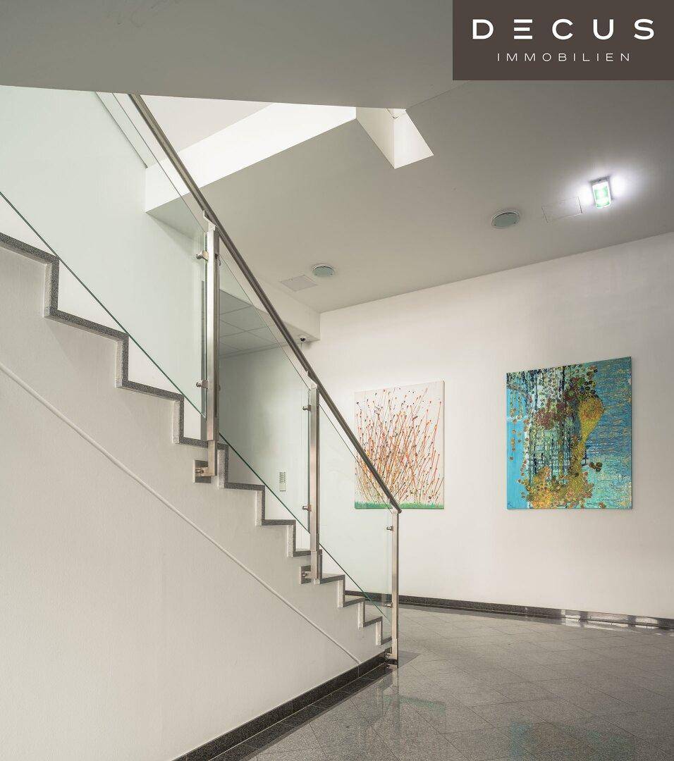 Modernes Treppenhaus mit Glasgeländer, Edelstahlhandlauf und Kunstwerken an den Wänden.