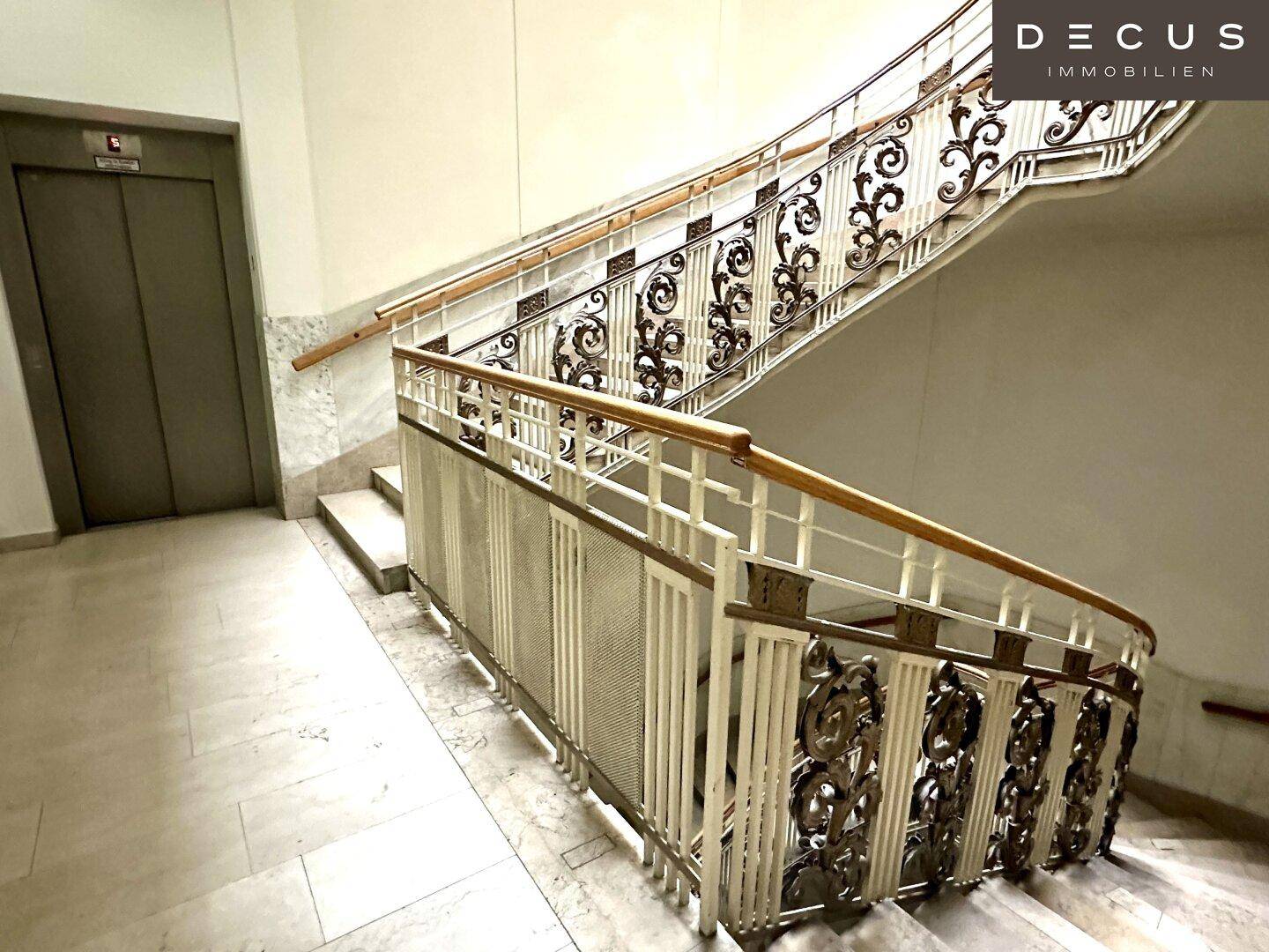 Geschwungene Treppe mit kunstvollem Geländer und Marmorstufen, führt zu den oberen Etagen.