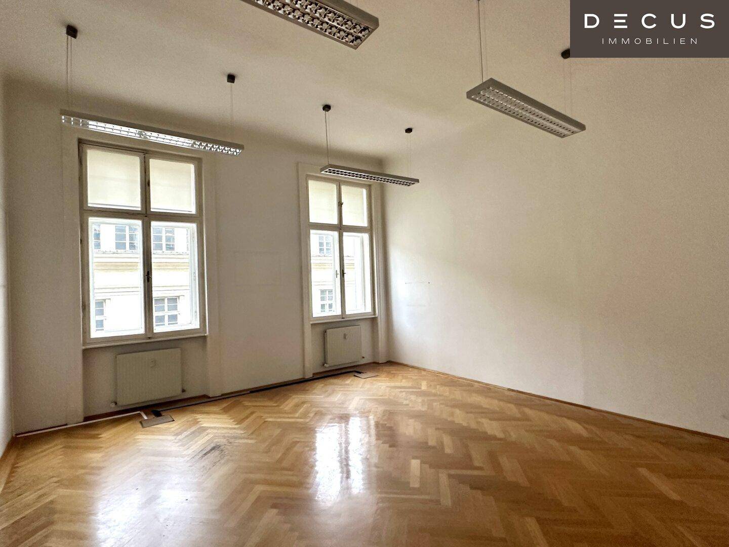Ruhiges Büro mit Fischgrätparkett und großen Fenstern, die für eine helle Umgebung sorgen.