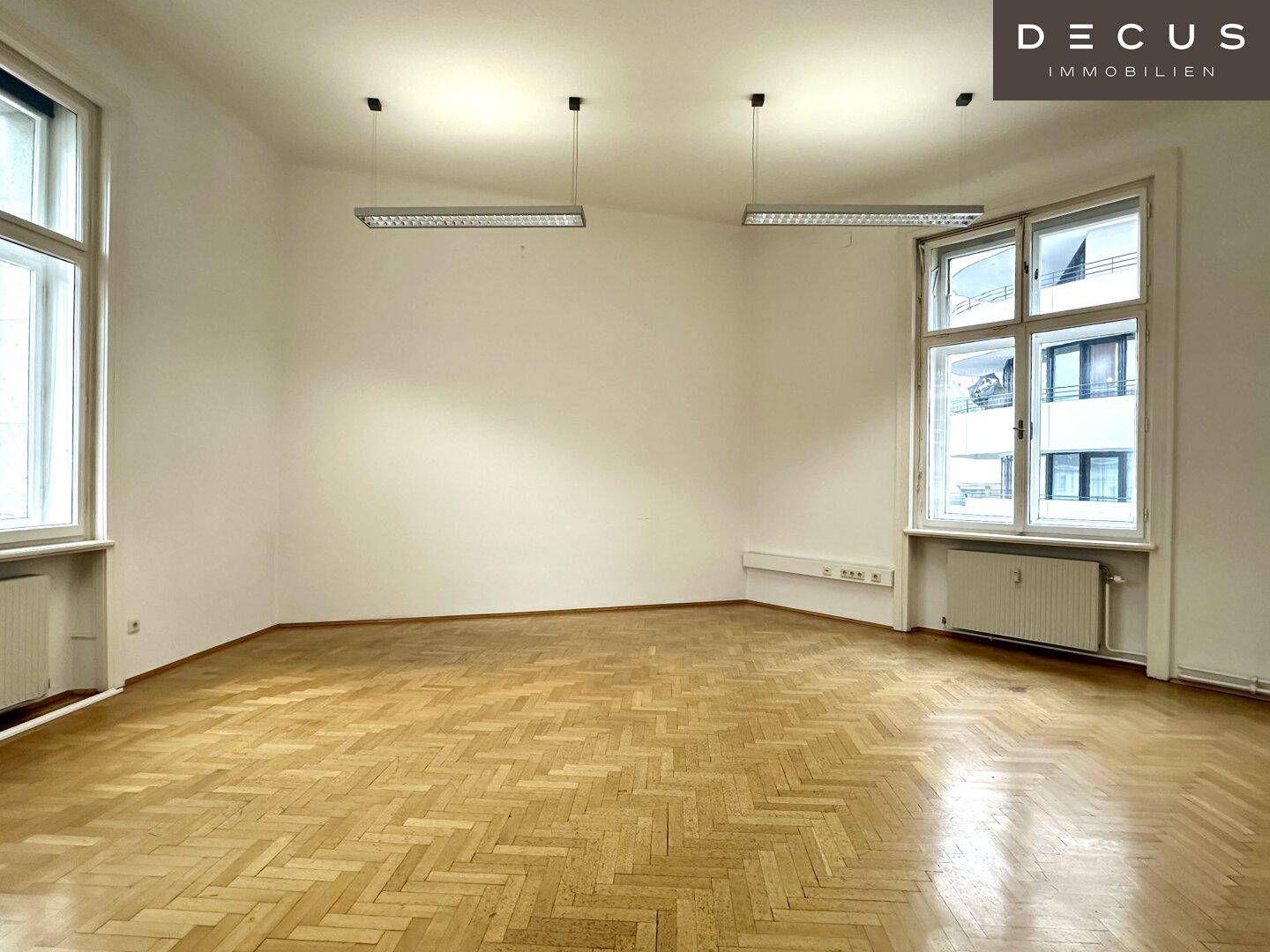 Eckbüro mit Fischgrätparkett und mehreren Fenstern, die viel Tageslicht hereinlassen.