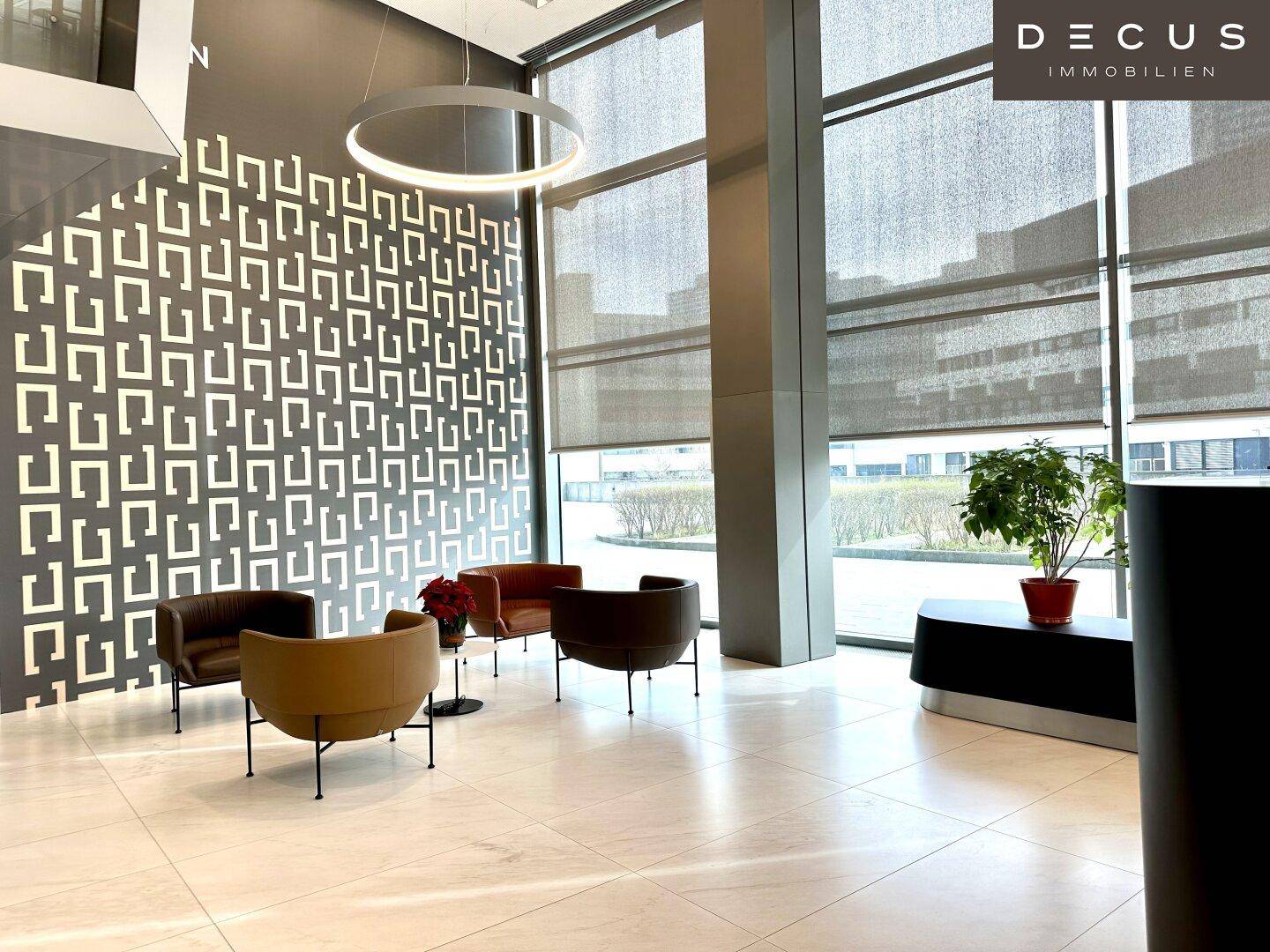 Moderner Wartebereich in einer stilvollen Lobby mit bequemen Sesseln, großen Fenstern und dekorativer Wandgestaltung.