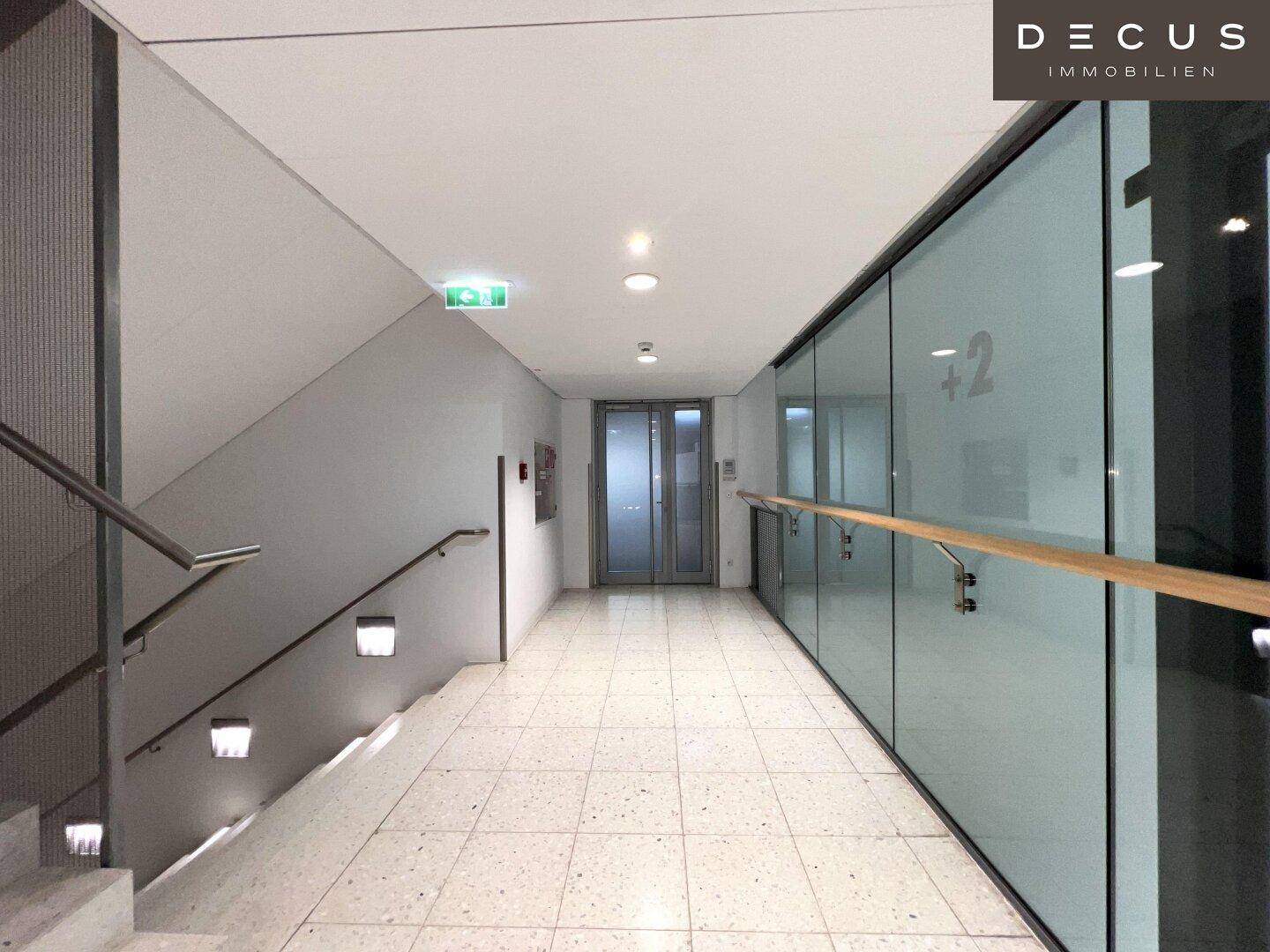 Heller Flur mit Treppenaufgang, Glaswänden und Terrazzoboden in einem modernen Bürogebäude.