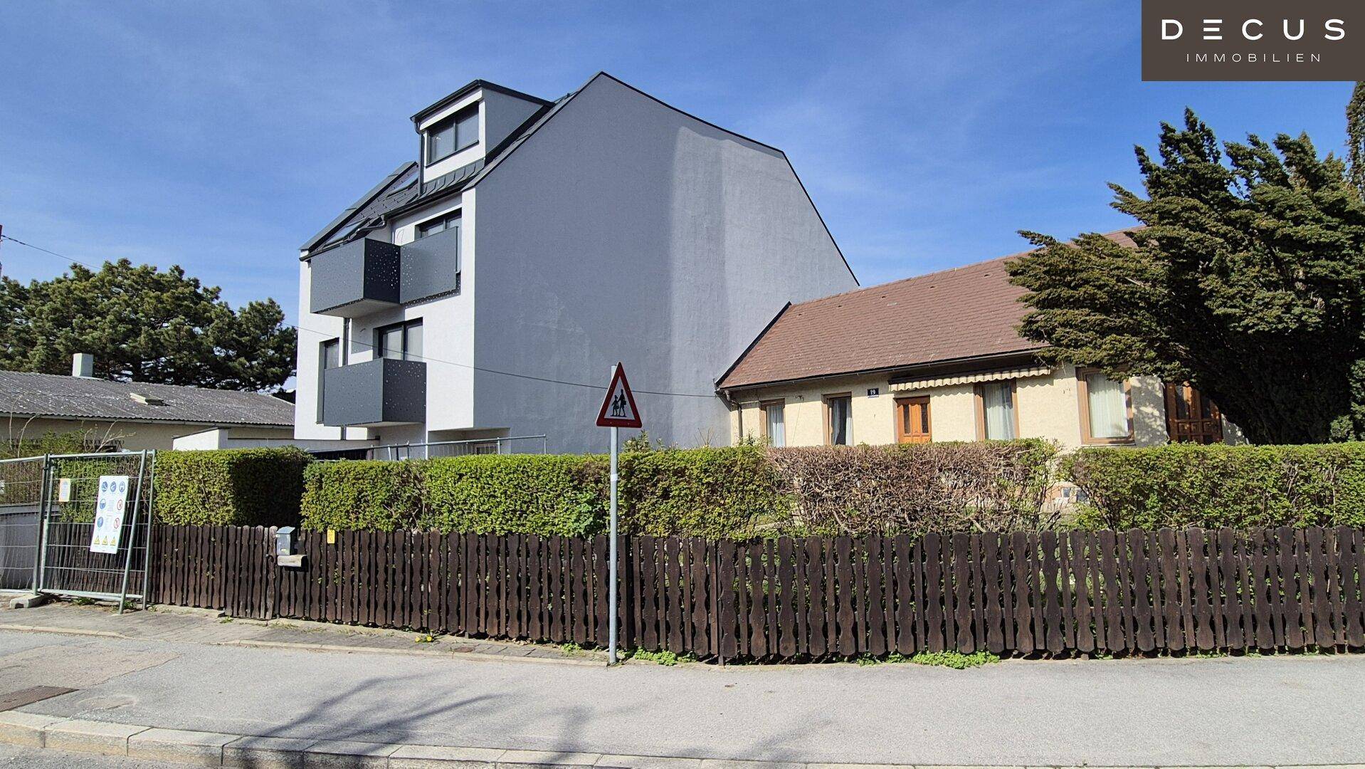 Ansicht des modernen Wohnhauses von der Straße mit Hecke und angrenzenden Gebäuden.