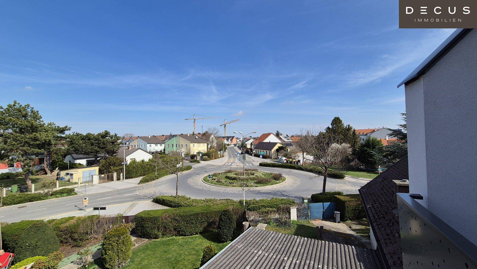Weitläufiger Blick über die Nachbarschaft mit Kreisverkehr und umliegenden Wohnhäusern unter blauem Himmel.