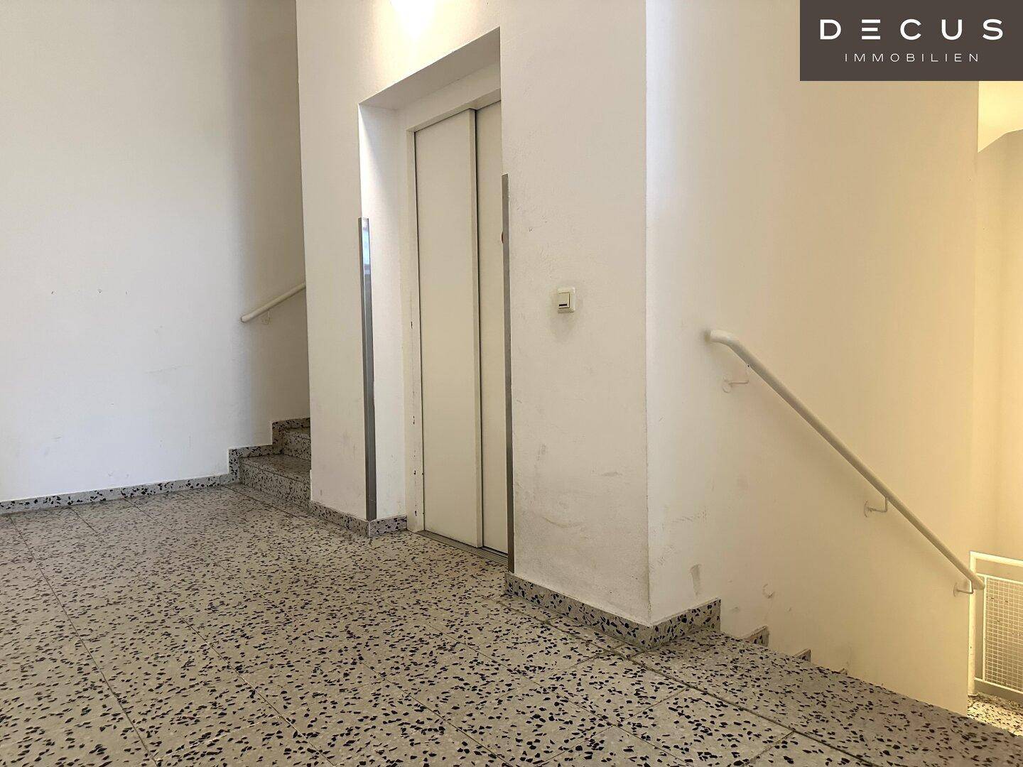 Treppenhaus mit Aufzug und Terrazzoboden, gut beleuchtet und gepflegt.