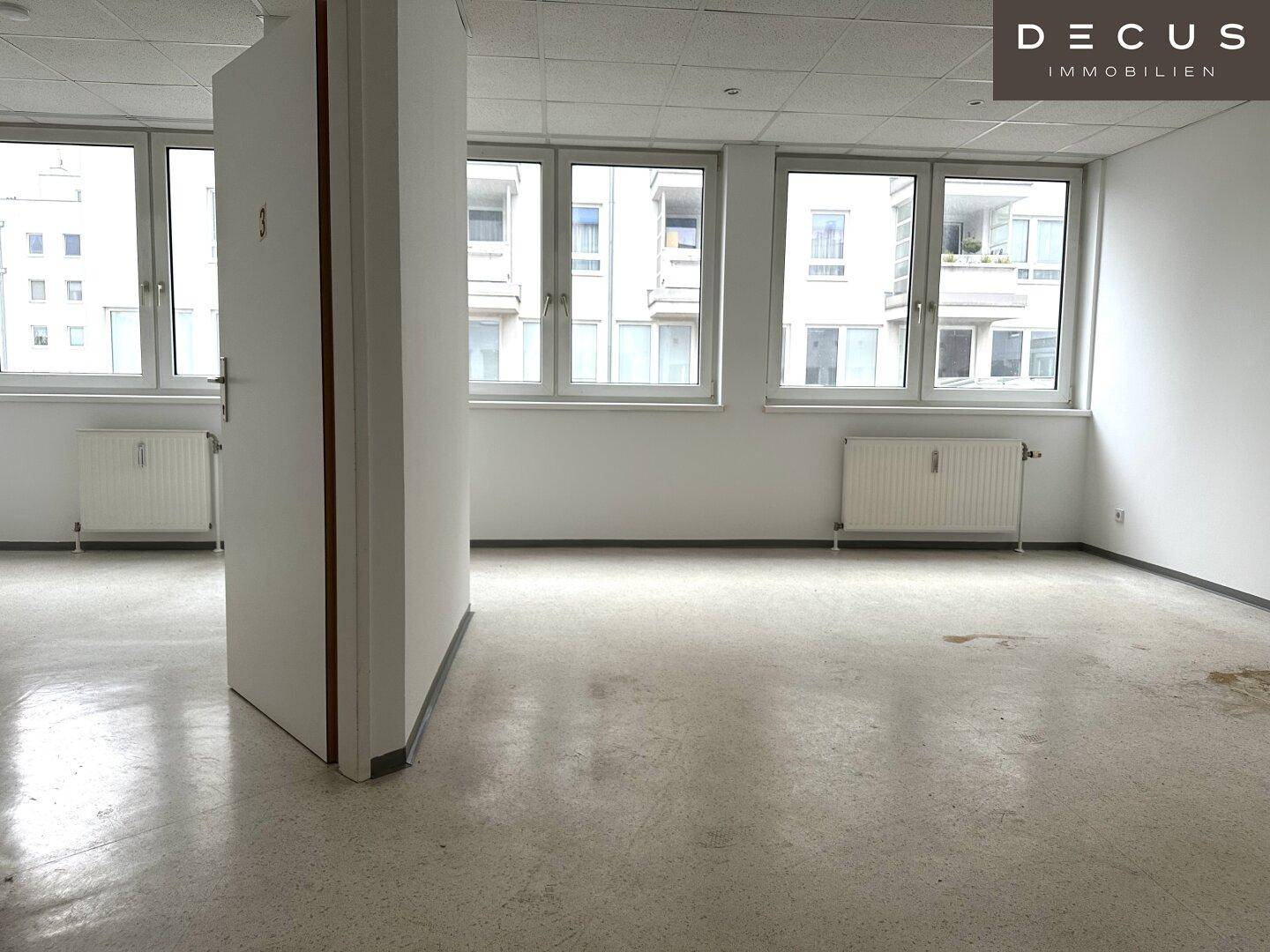 Geräumiger, leerer Bürobereich mit großen Fenstern und Blick auf die Umgebung.