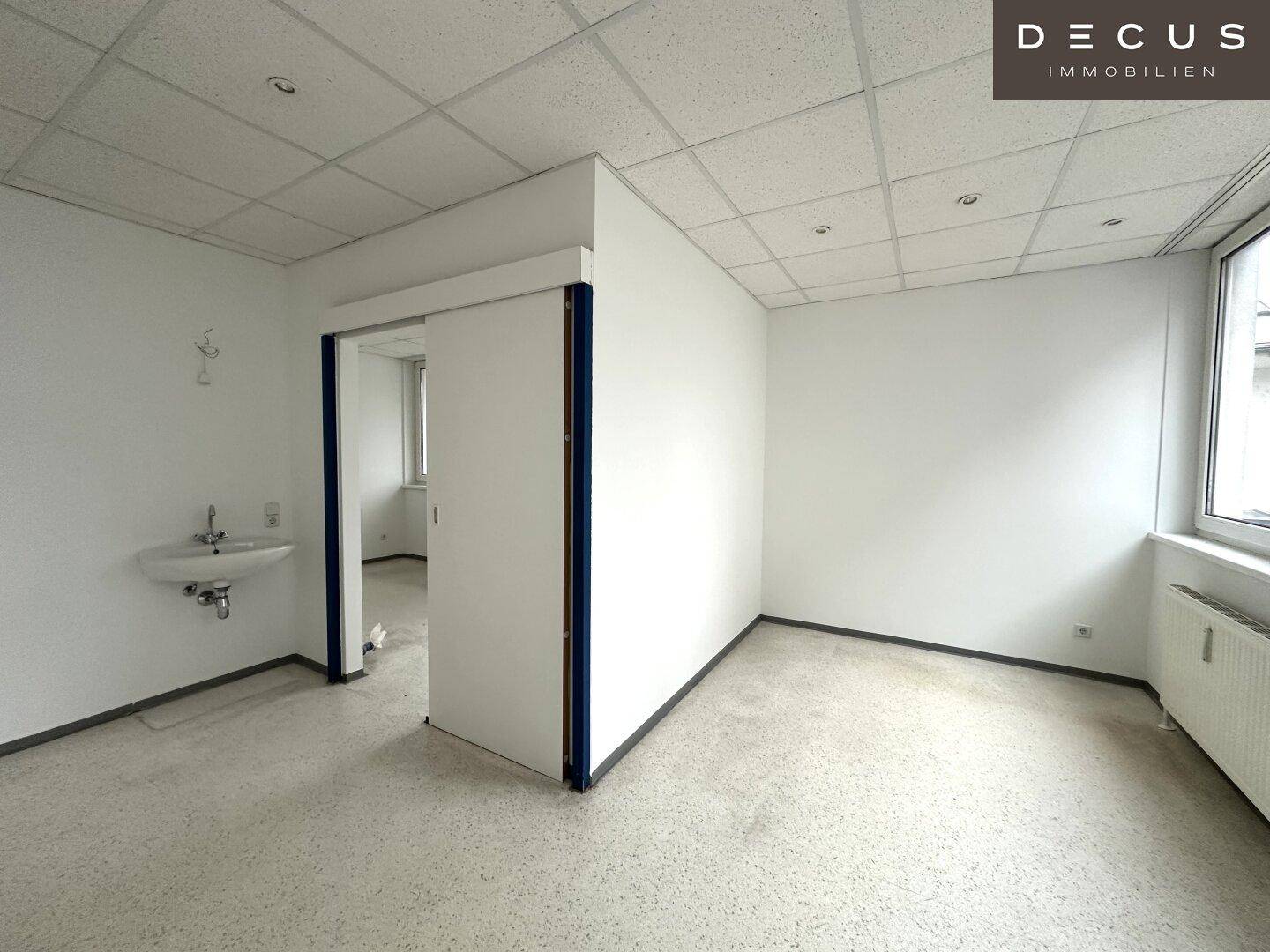 Leerer Büroraum mit Waschbecken und Schiebetür, bereit für individuelle Einrichtung.