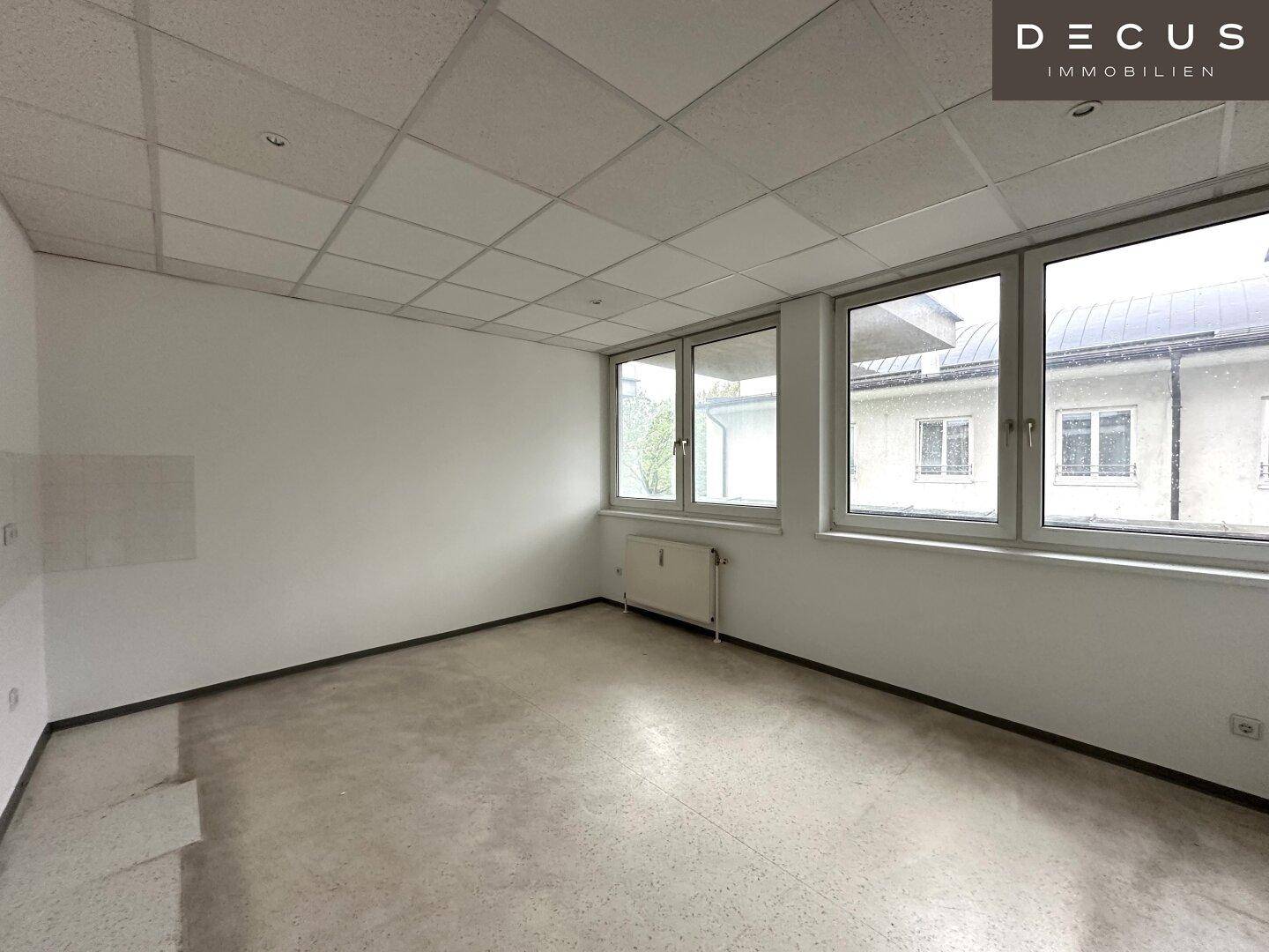 Leerer Büroraum mit großen Fenstern und einem Heizkörper, bereit für individuelle Gestaltung.