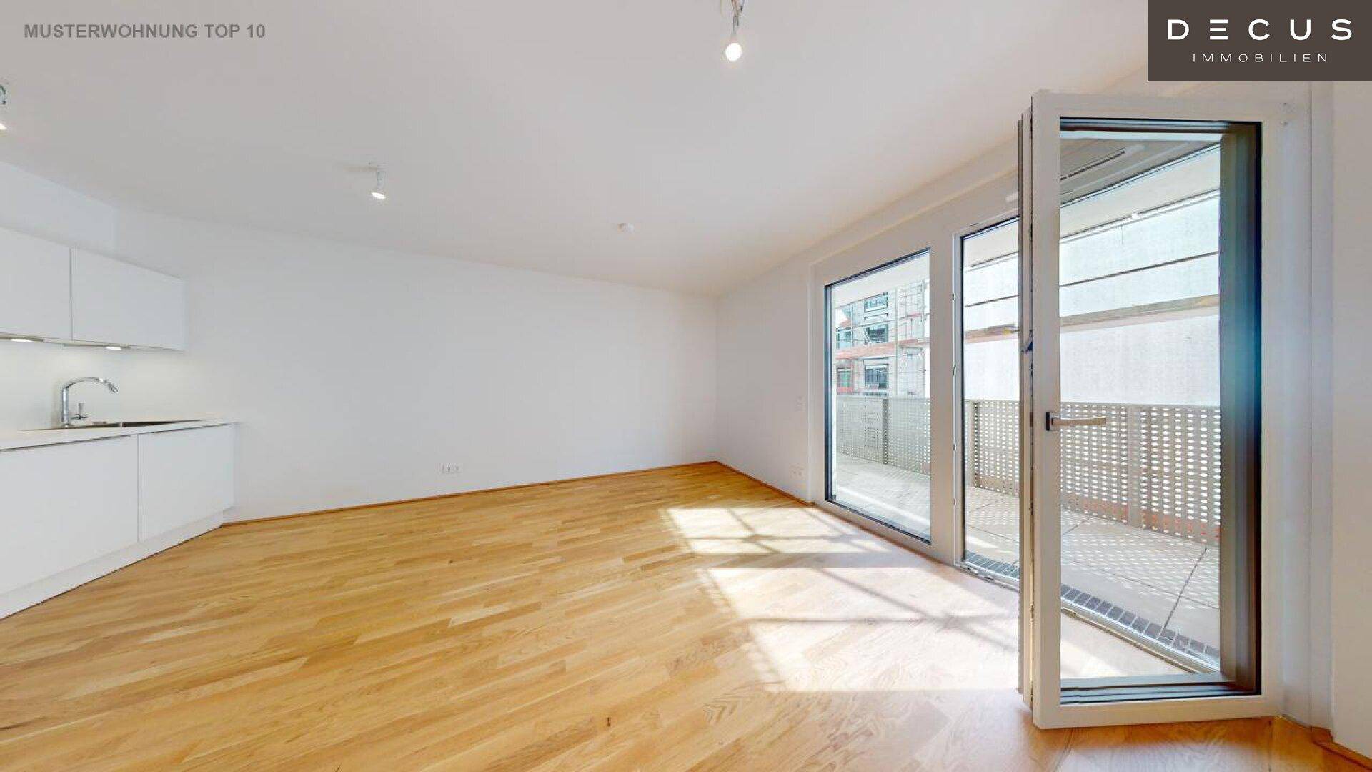 Heller Wohnbereich mit offener Küchenzeile, Parkettboden und Zugang zum Balkon.
