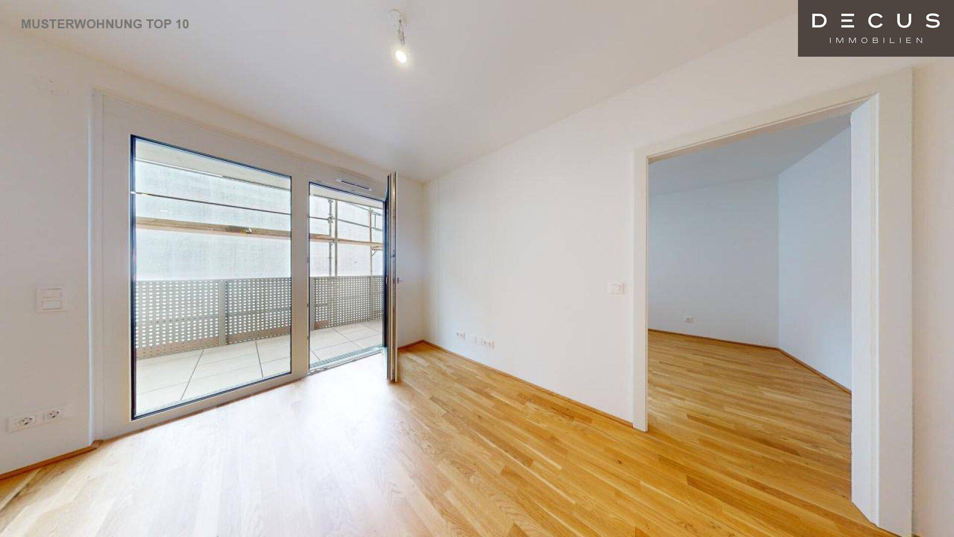 Geräumiger Wohnbereich mit Parkettboden und großen Fenstern zum Balkon.