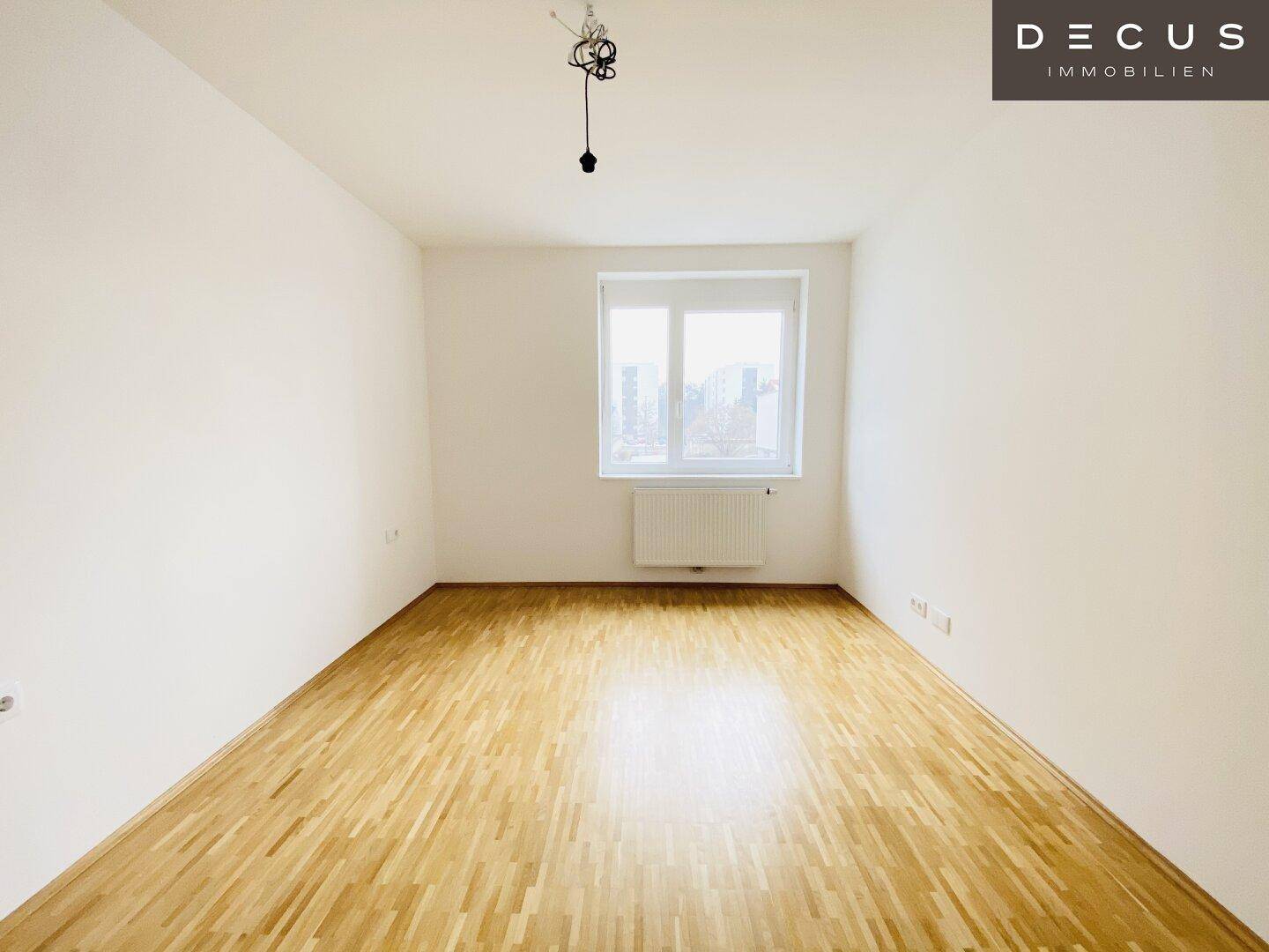 Leeres Schlafzimmer mit hellem Parkettboden und großem Fenster, bereit zur individuellen Gestaltung.
