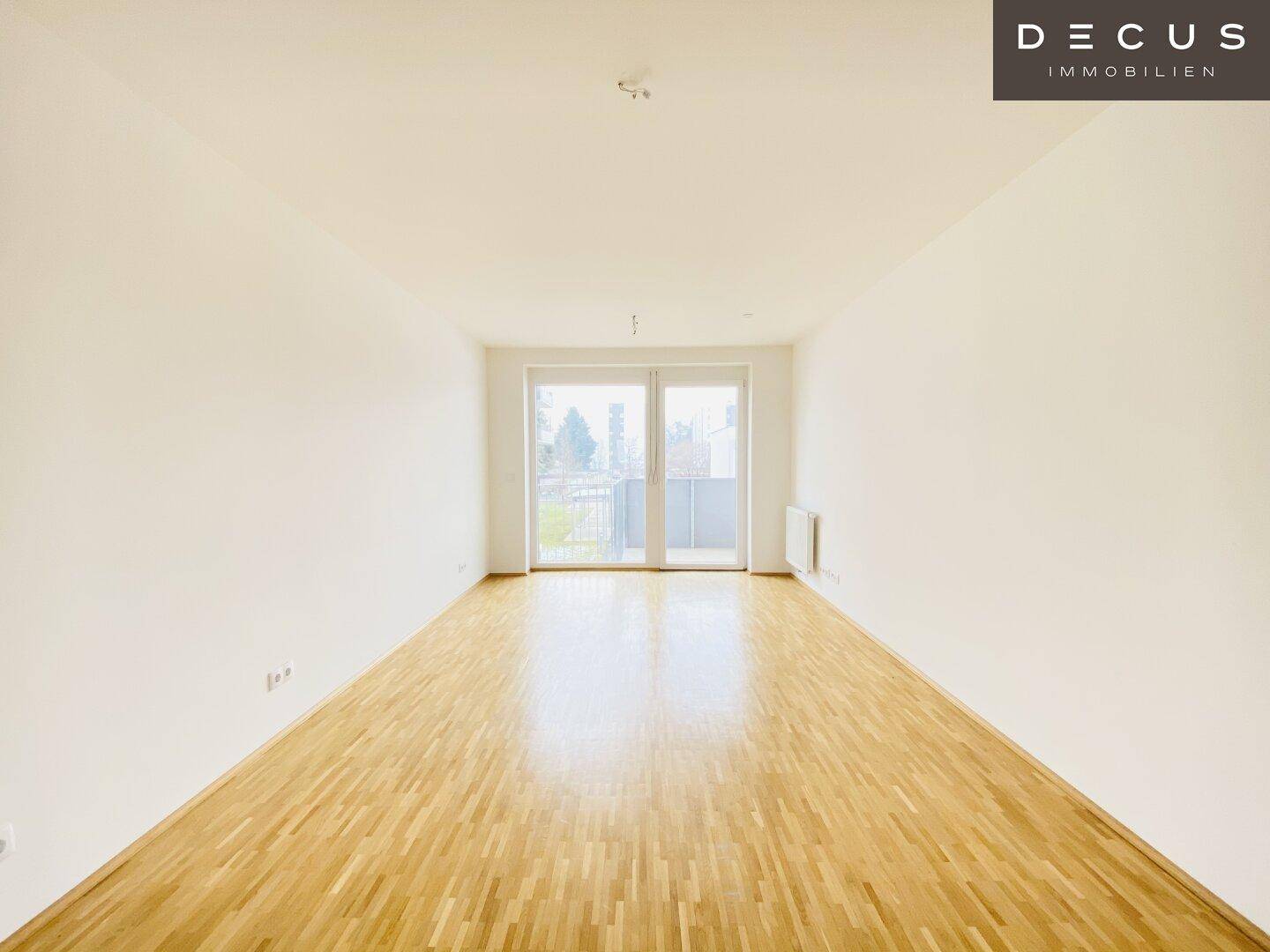 Heller Wohnraum mit Parkettboden und großen Fenstern, die viel Tageslicht hereinlassen.