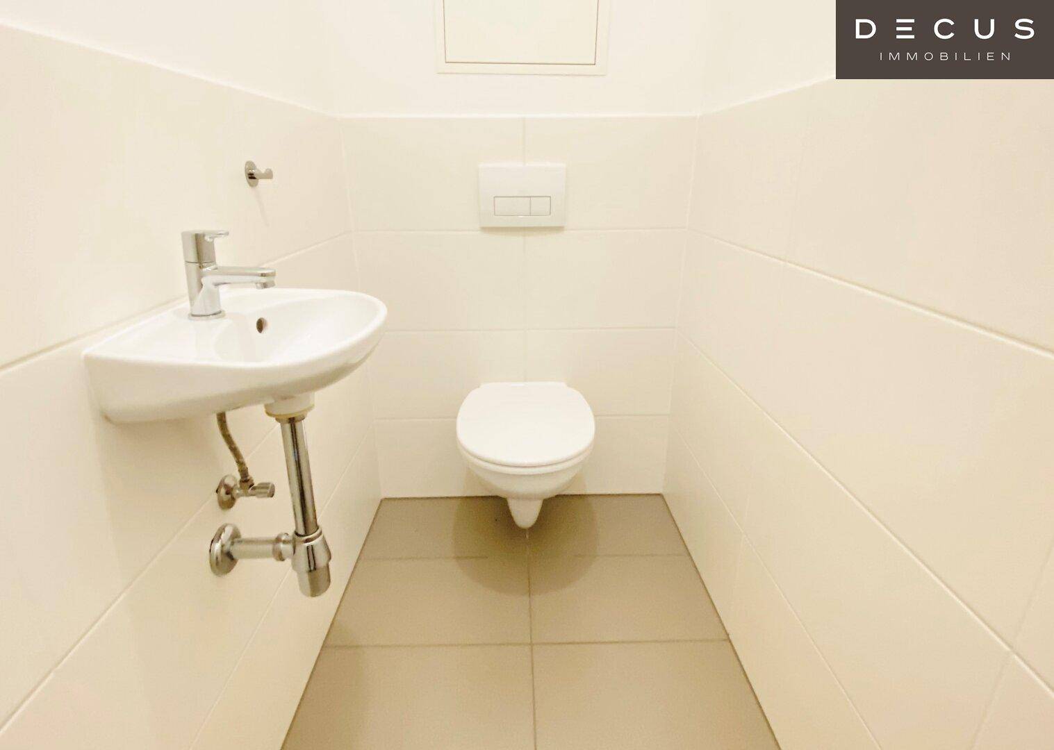 Kleines Gäste-WC mit wandhängendem WC, Waschbecken und hellen Fliesen an Wänden und Boden.