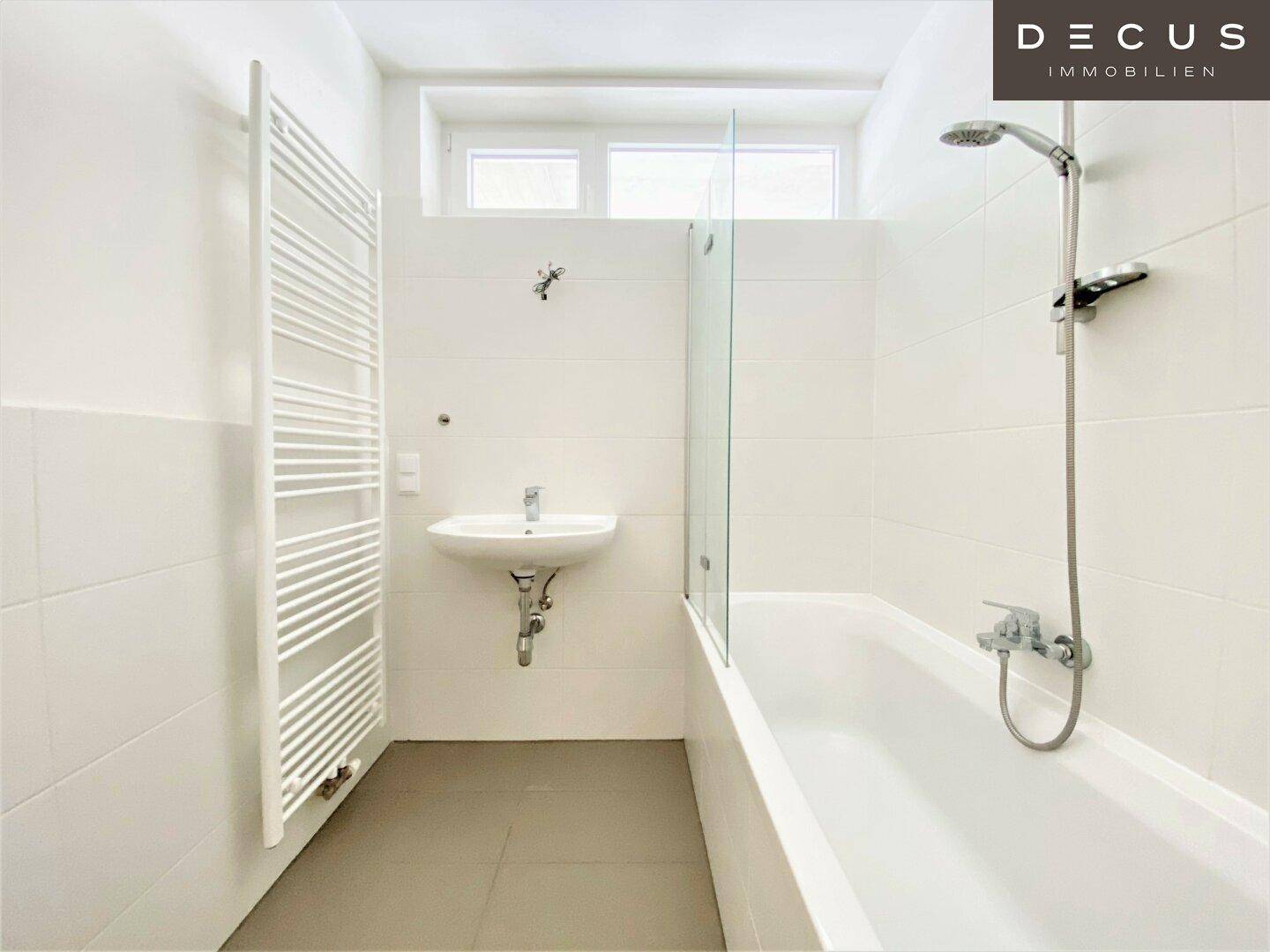 Helles Badezimmer mit Badewanne, Duschvorrichtung, Waschbecken und beheiztem Handtuchhalter.