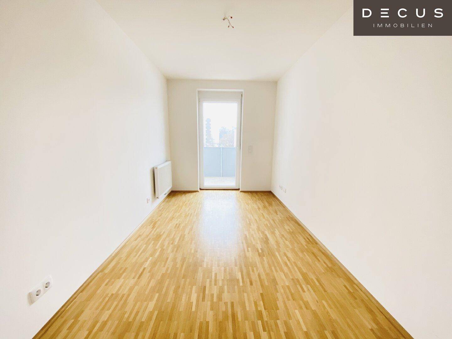 Leeres Zimmer mit Parkettboden und Zugang zu einem Balkon, ideal als Schlaf- oder Arbeitszimmer.