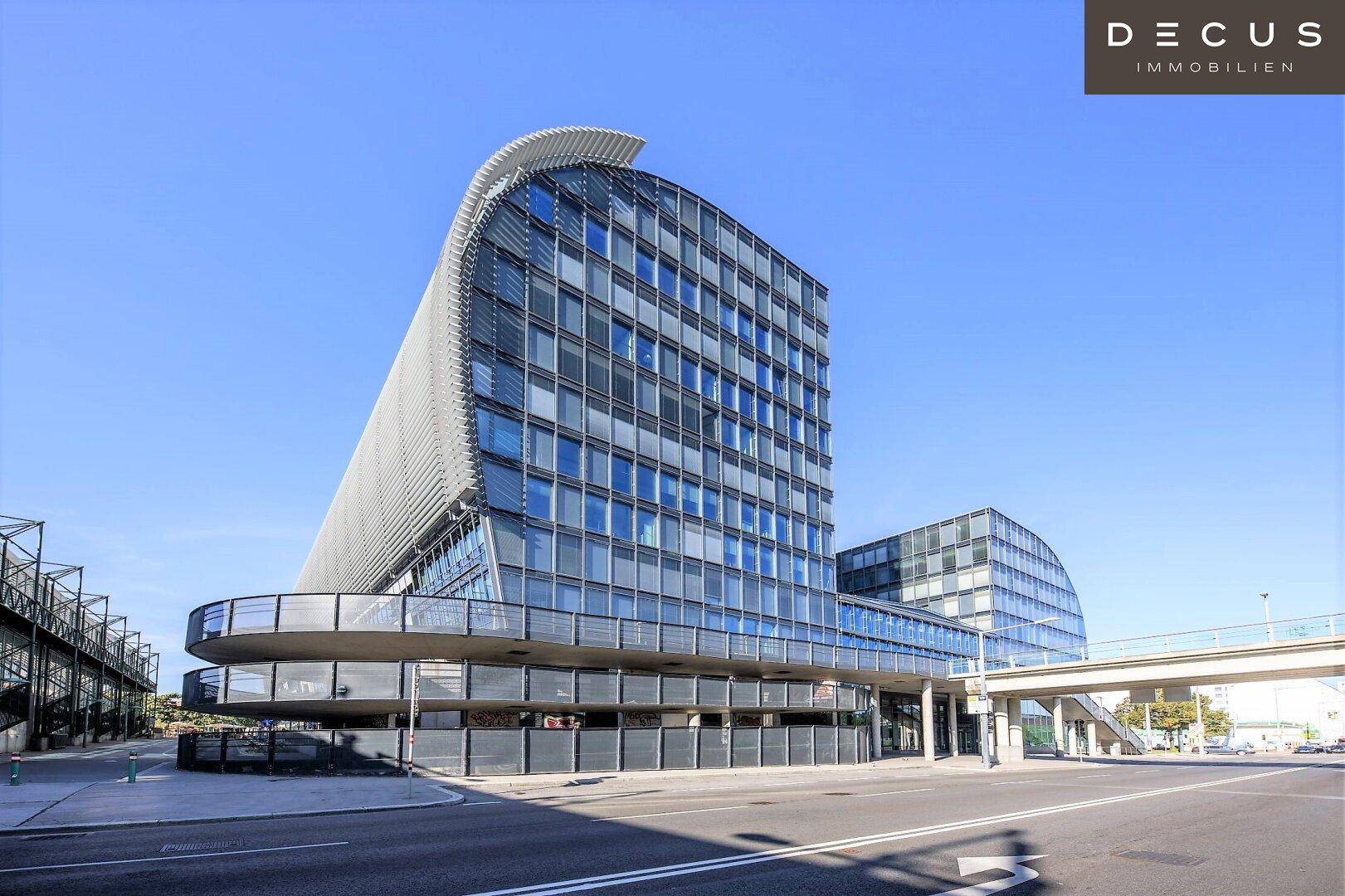 Ansicht eines modernen Bürokomplexes mit markanter Glasfassade und geschwungenen Linien an einem sonnigen Tag.