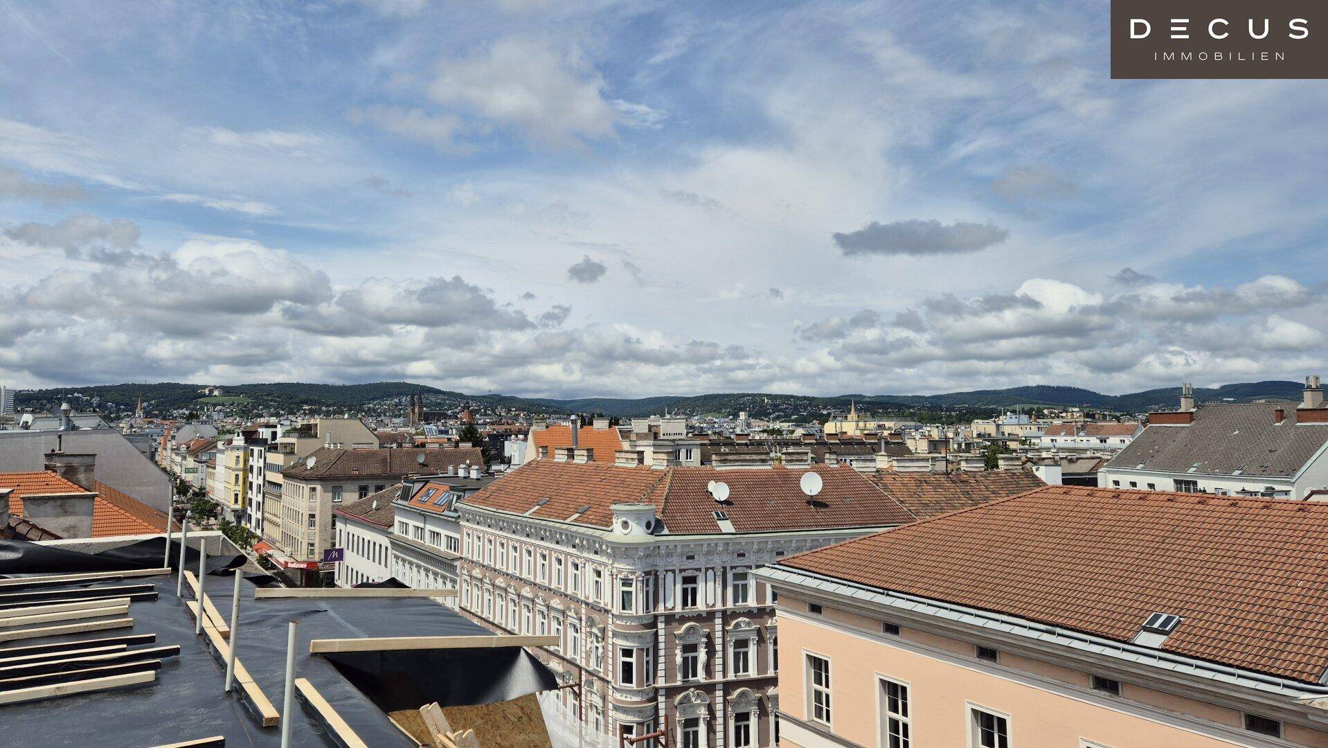 Weitläufiges Stadtpanorama mit Blick über Dächer und entfernte Hügel unter bewölktem Himmel, im Vordergrund ein Flachdach im Bau.