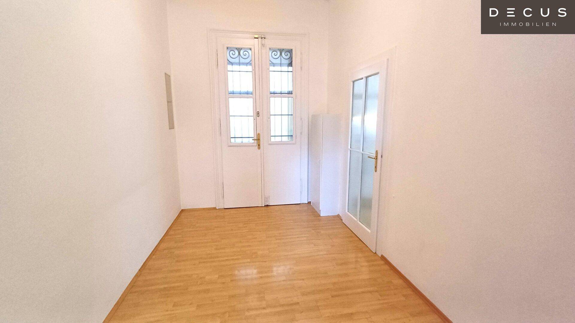 Heller Raum mit Holzboden und zwei Türen, eine davon mit dekorativem Glas und Sprossen.