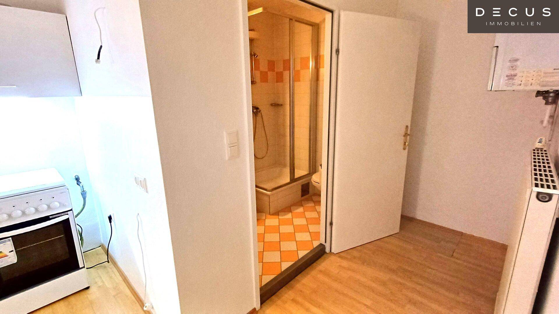 Blick von der Küchenzeile auf den Eingang zum Badezimmer mit Duschkabine und Fliesenboden.