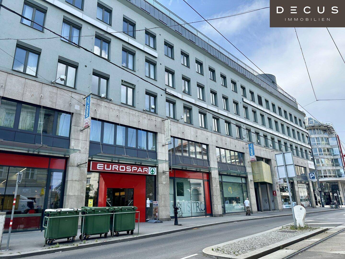 Erdgeschossansicht eines Geschäftsgebäudes mit verschiedenen Ladenfronten, darunter ein Supermarkt und ein Restaurant.