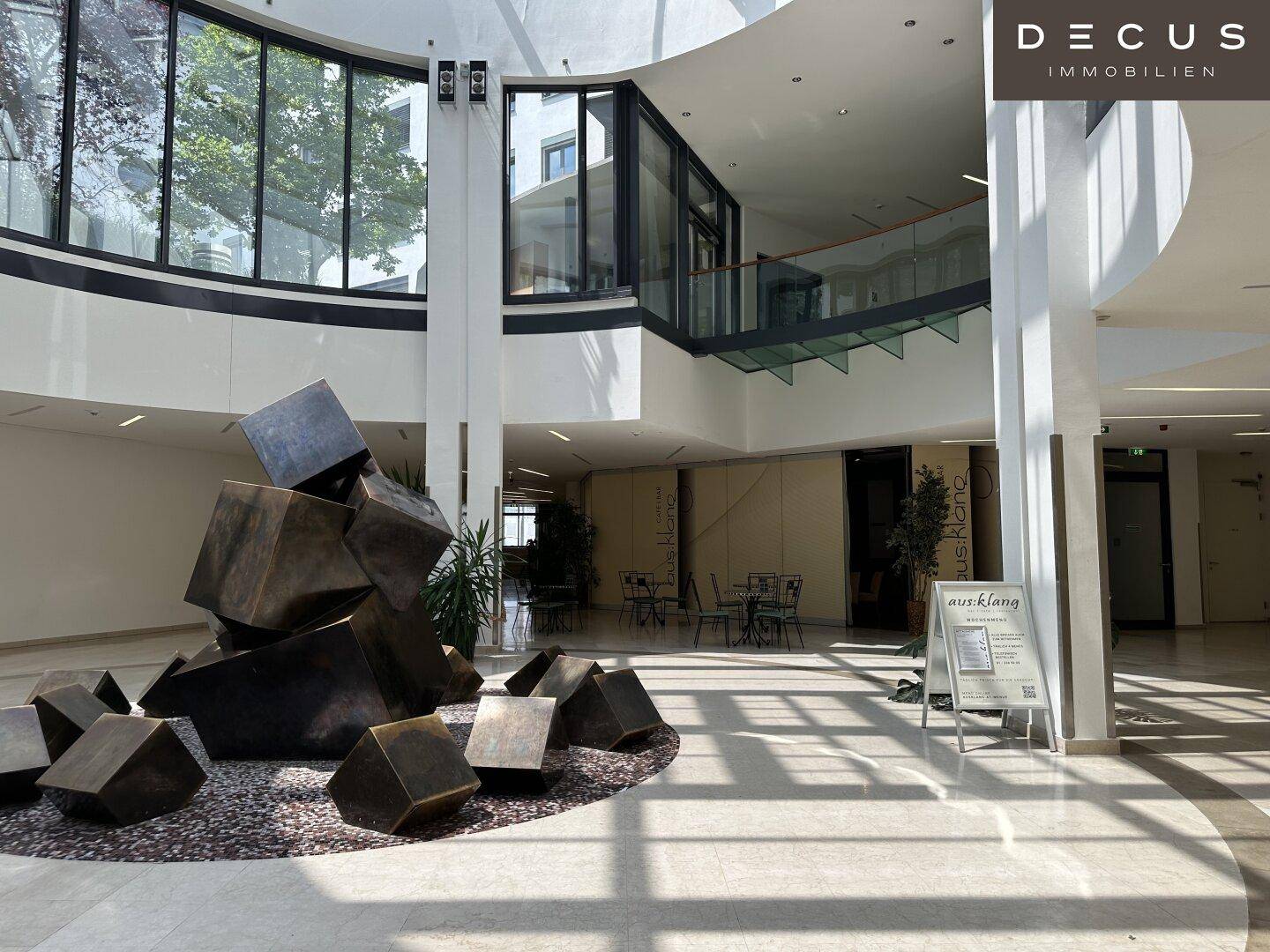Panoramablick auf das Atrium mit seiner beeindruckenden Glasdachkonstruktion und der offenen Galerie im Obergeschoss.