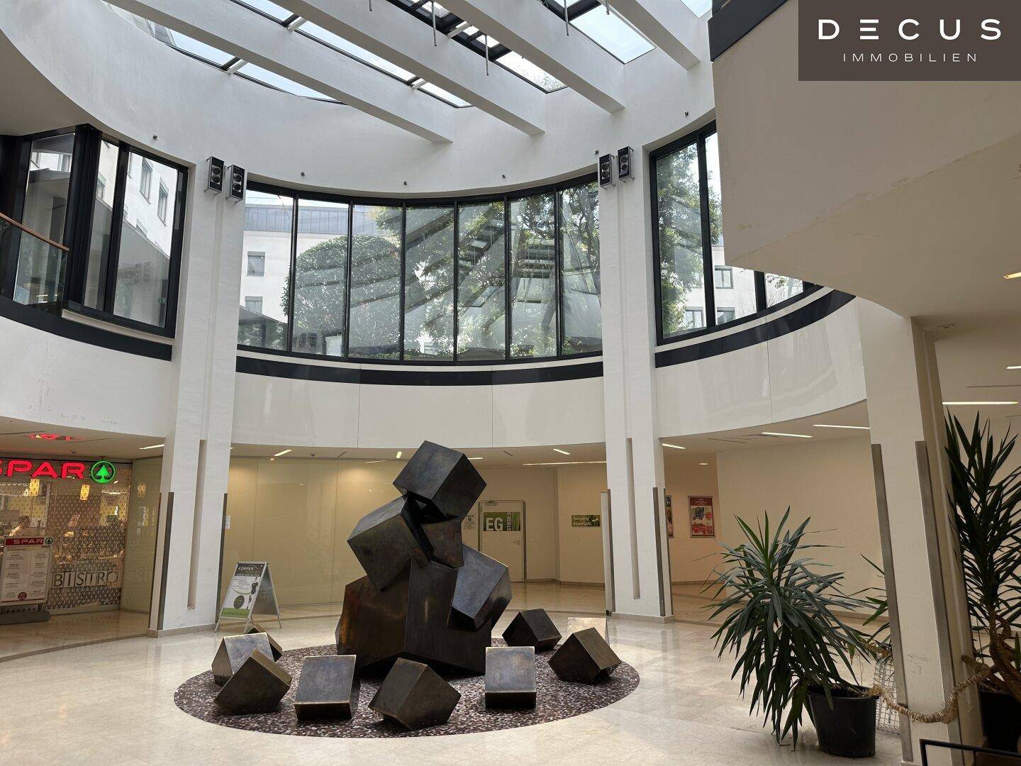 Weitläufiges Atrium mit beeindruckender Skulptur und einer geschwungenen Glasfassade, die viel Licht hereinlässt.