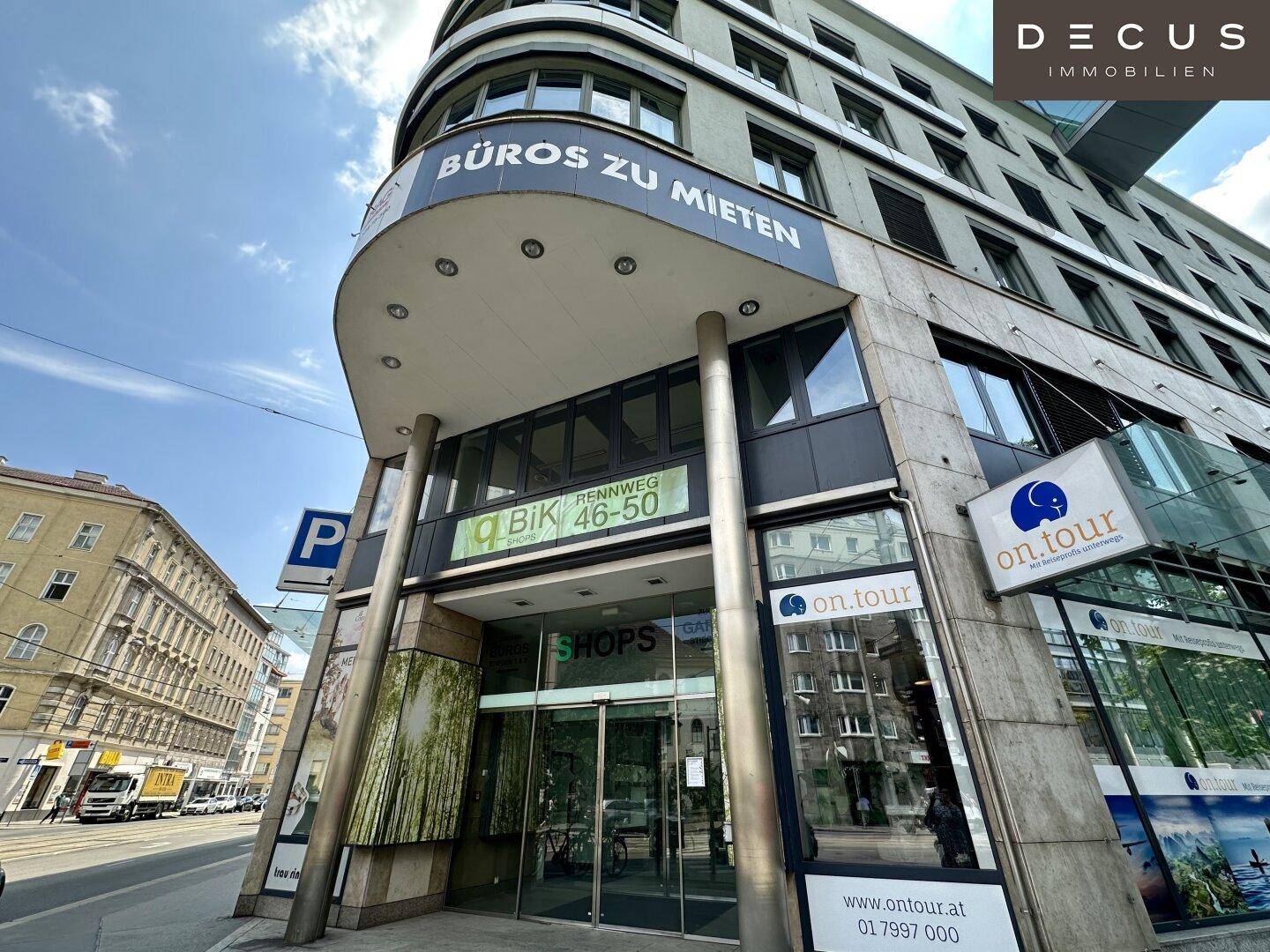 Eingangsbereich eines modernen Büro- und Geschäftsgebäudes mit großen Glasfronten und Beschilderung.