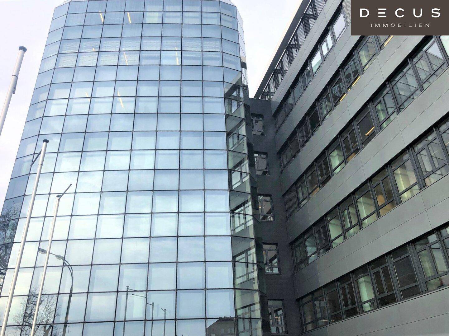 Ansicht von zwei modernen Bürogebäuden, eines mit geschwungener Glasfassade und das andere mit grauer Fassade.