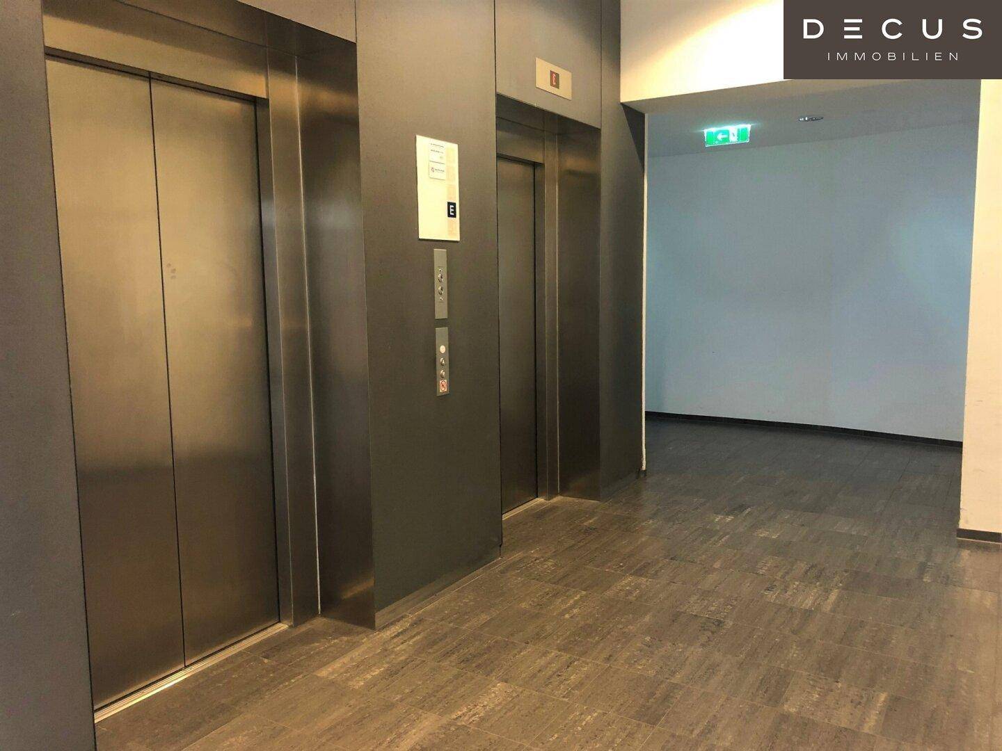 Moderner Flur mit zwei Aufzügen und dunklen Fliesen, der Zugang zu den oberen Etagen bietet.