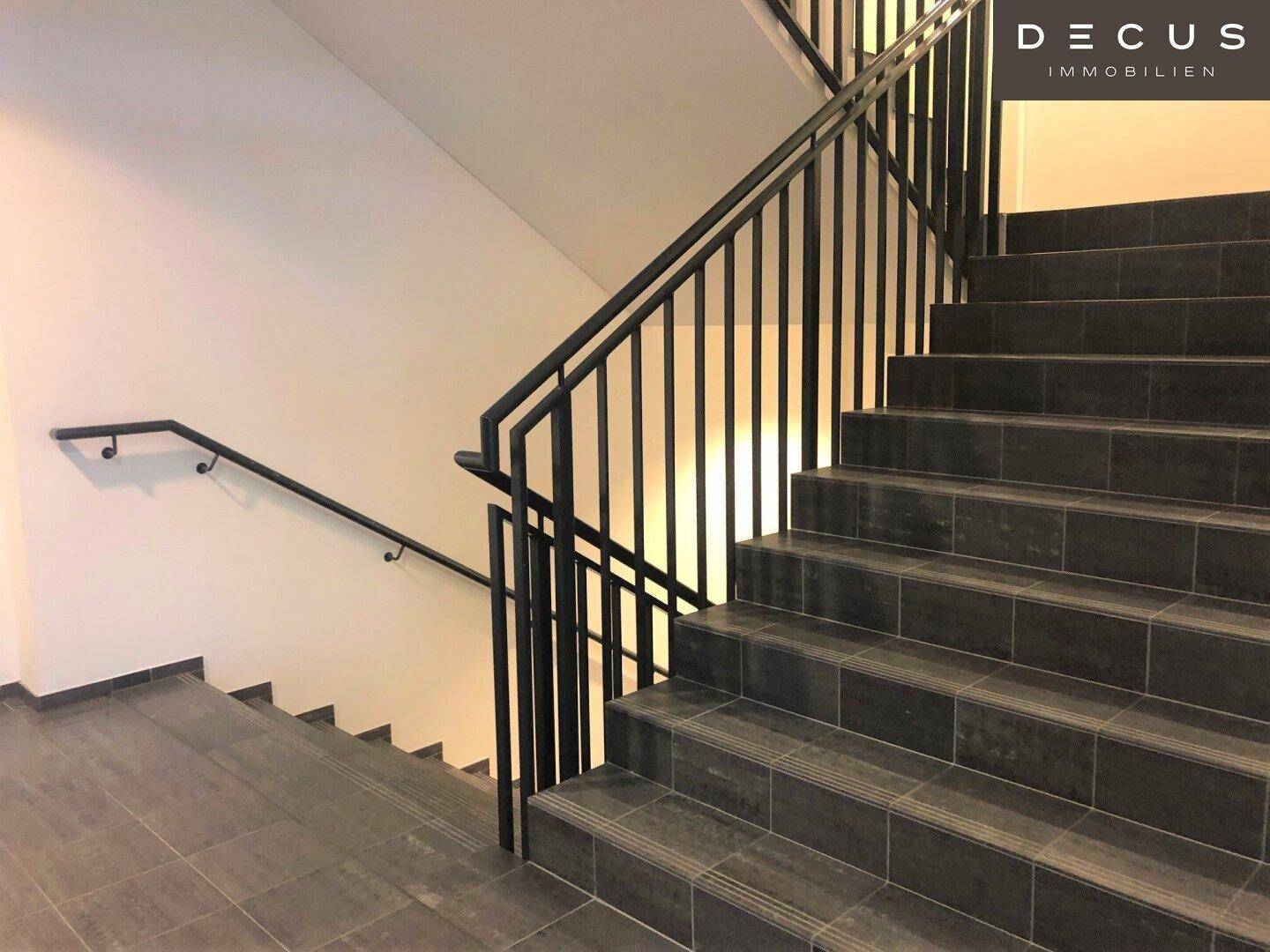 Modernes Treppenhaus mit dunklen Fliesenstufen und einem schlichten schwarzen Metallgeländer.